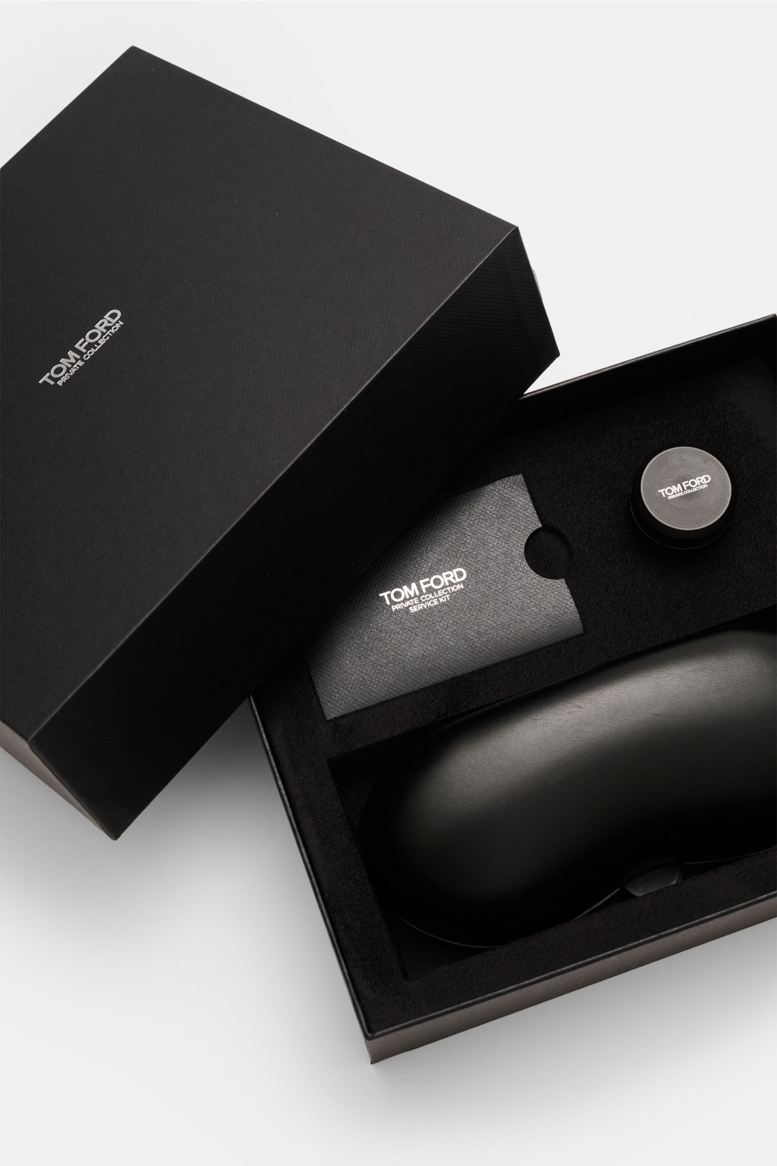 Schwarze Tom Ford Horn Brille 'Private Collection' schwarz/grau/hellbraun gemustert in geöffneter Box mit Lederetui, Politurset und Putztuch, Draufsicht.