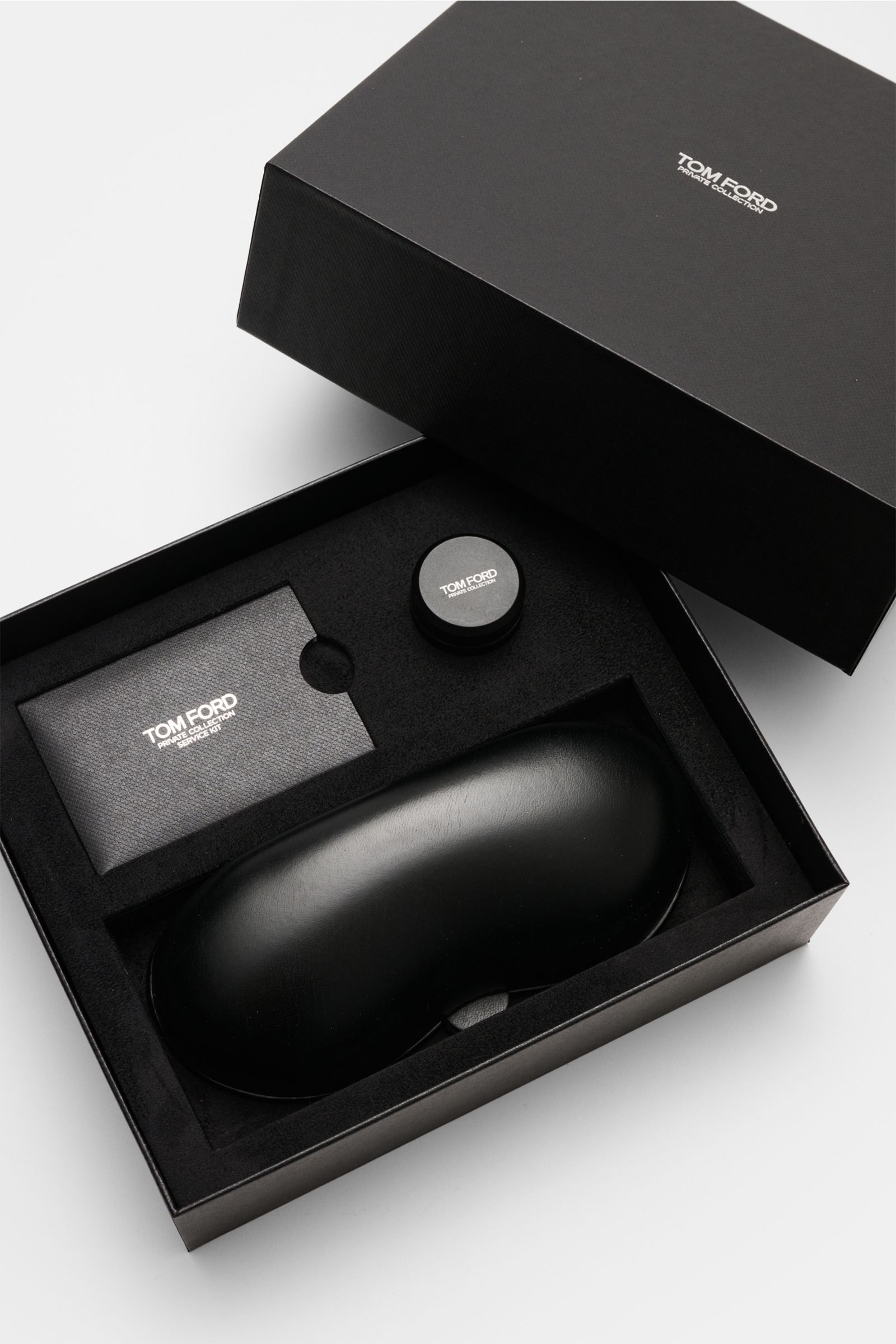 Top-down view of the Tom Ford Horn Brille 'Private Collection' schwarz/grau gemustert packaging including a black leather hard case, polishing set, and cleaning cloth, highlighting its exclusive horn frame, rectangular shape, blue light filter lenses, and