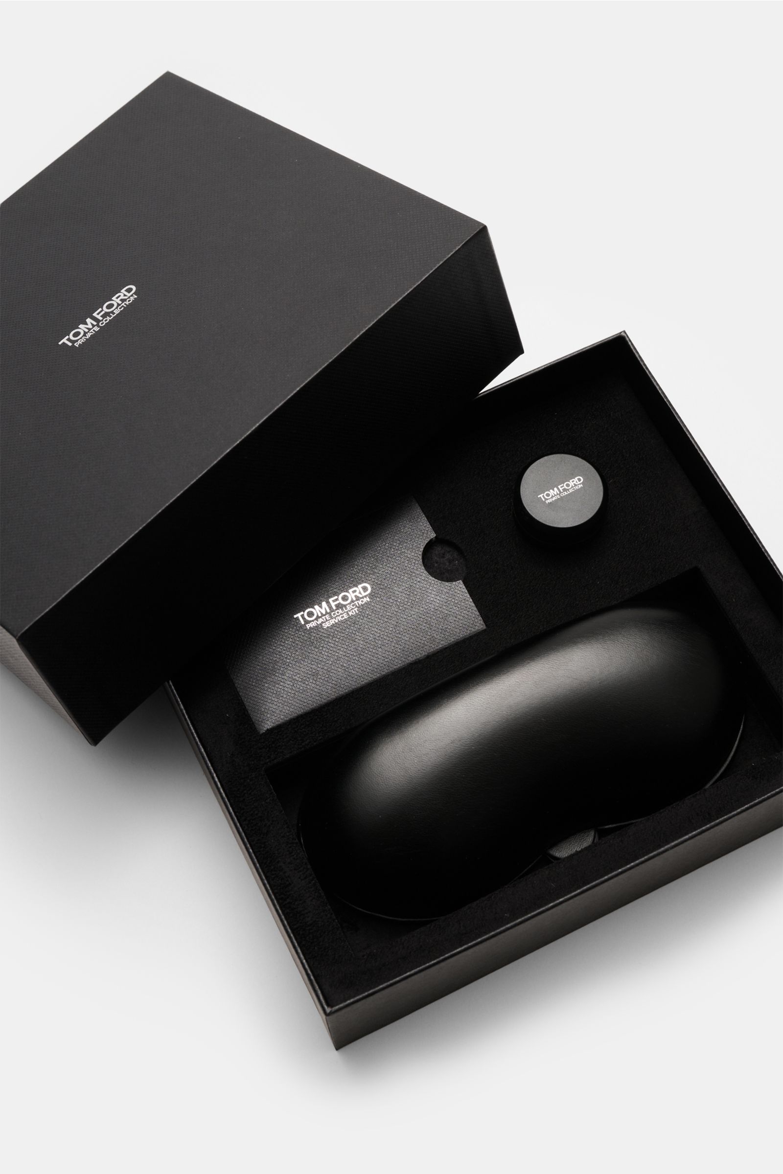 Top-down view of Tom Ford Horn Brille 'Private Collection' schwarz/braun/sand gemustert packaging including leather hard case, horn polish set, and cleaning cloth. Stilvoller Eyecatcher: Die exklusive Horn Brille aus der 'Private Collection' von TOM FORD 