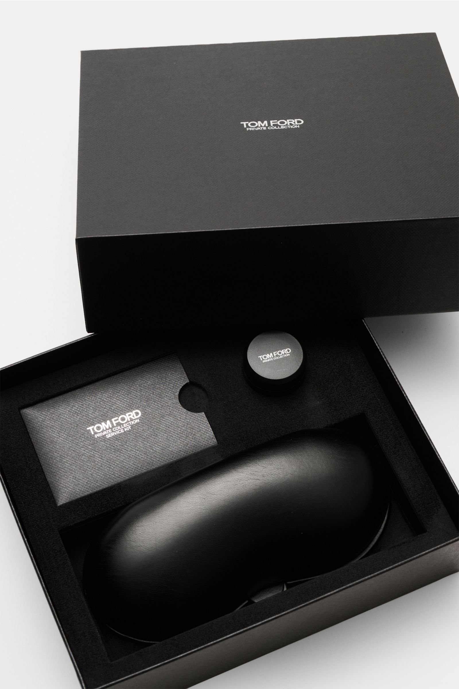 Top-down view of the black Tom Ford Horn Brille 'Private Collection' schwarz/grau gemustert packaging including leather hard case, polishing kit, and cleaning cloth.
