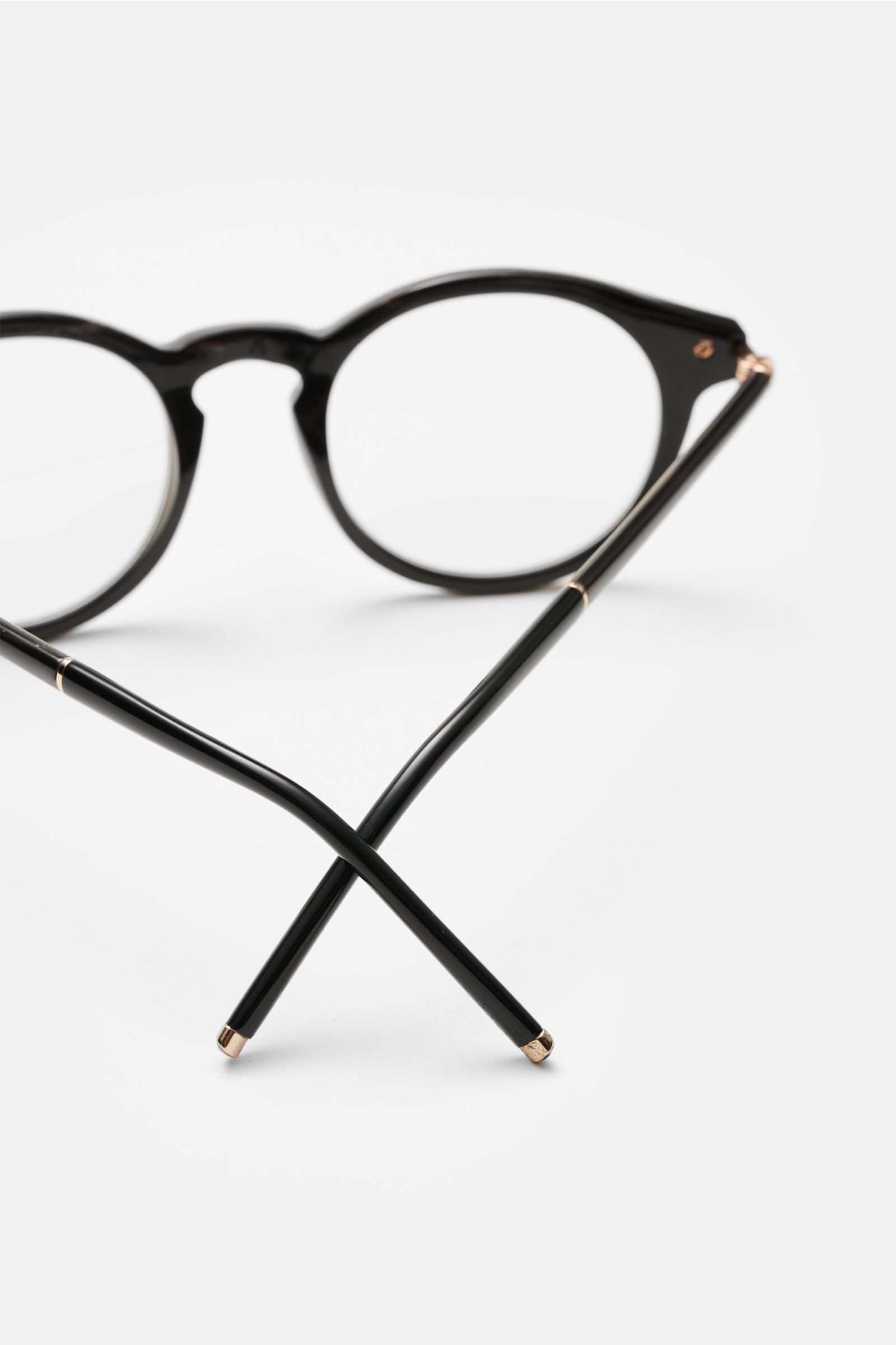 Tom Ford Horn Brille 'Private Collection' schwarz/graubraun/weiß gemustert seen from front with crossed temple arms, stylish round horn frame with blue light filter lenses, T-shaped details, includes leather hard case, horn polish set and cleaning cloth. 