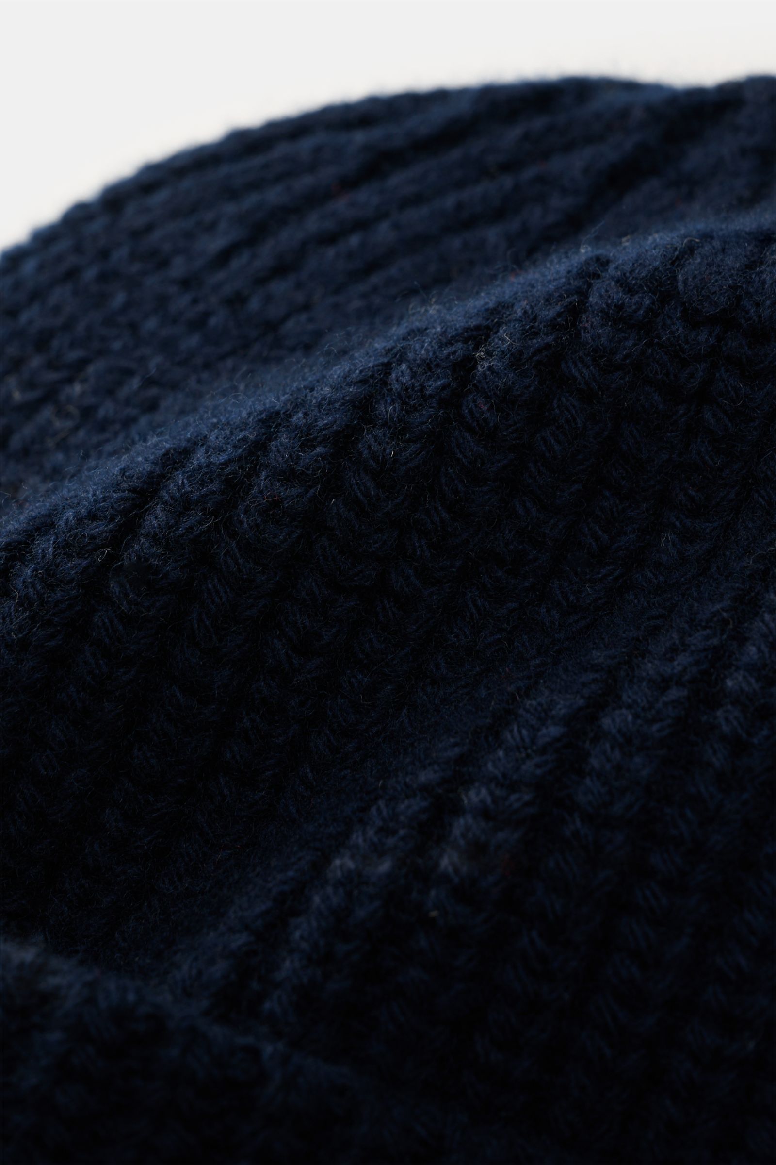 Nahaufnahme der Stone Island Wollmütze navy aus reiner Wolle, leicht griffig, Rippstrick, breiter Umschlag mit STONE ISLAND-Weblabel vorne.