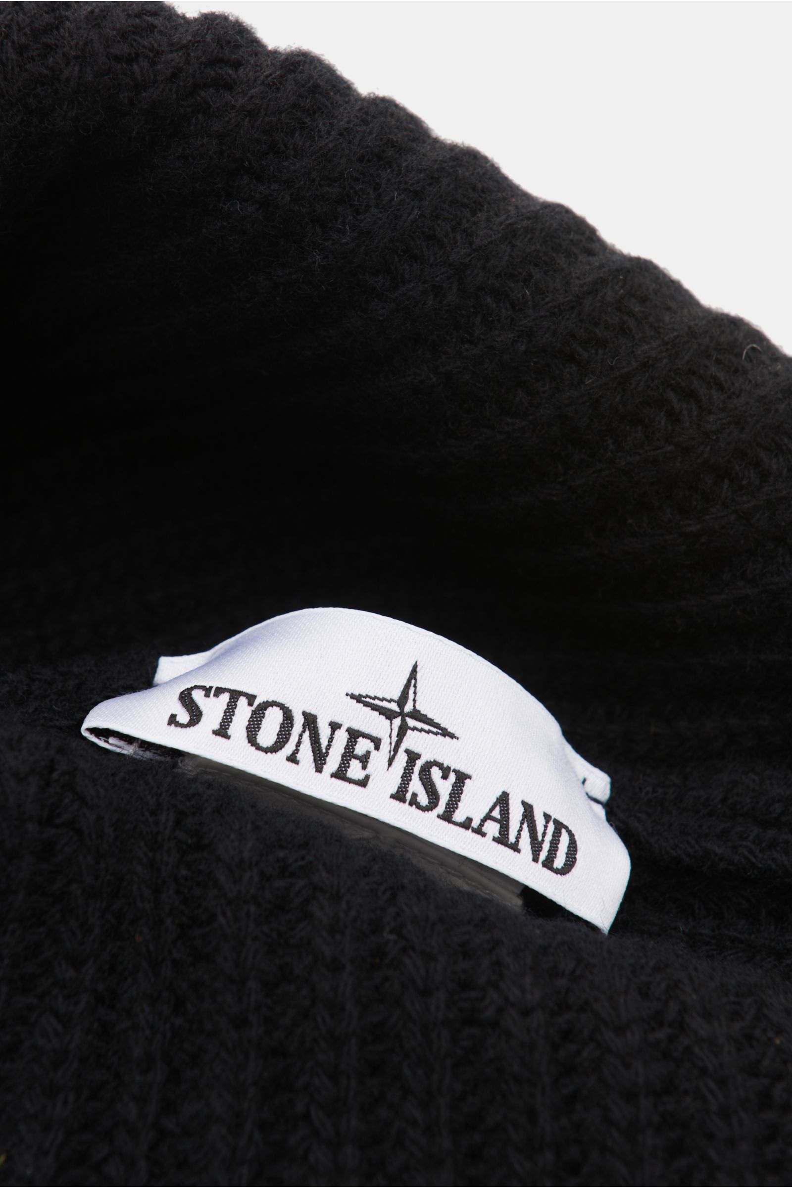Stone Island Wollmütze schwarz aus reiner Wolle, leicht griffig, moderne Rippstrick-Optik, breiter Umschlag, Front mit STONE ISLAND-Weblabel, Nahaufnahme.
