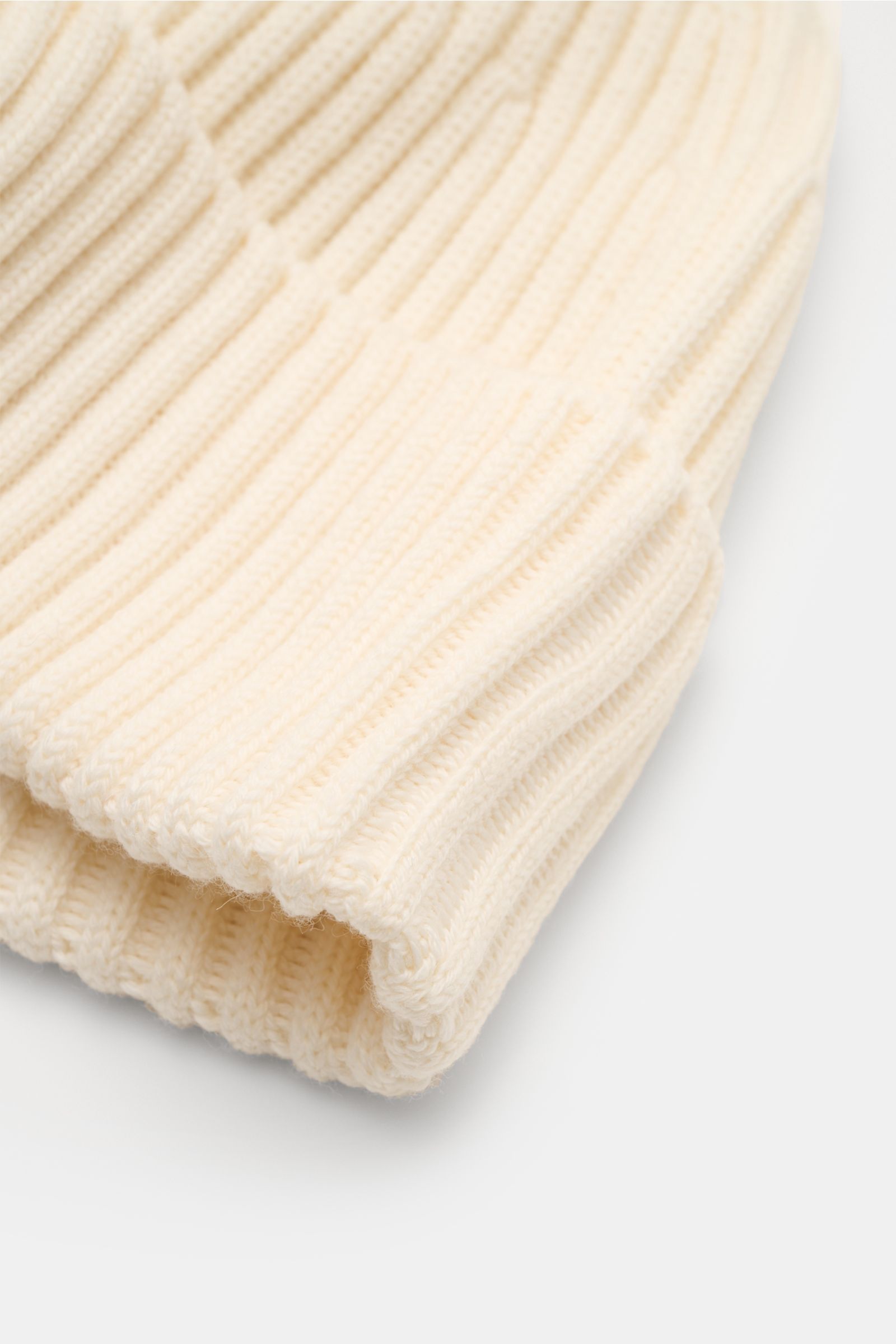 Stone Island Wollmütze creme aus reiner Wolle, weicher Griff, moderne Rippstrick-Optik, breiter Umschlag, Front mit STONE ISLAND-Weblabel, Nahaufnahme von oben.