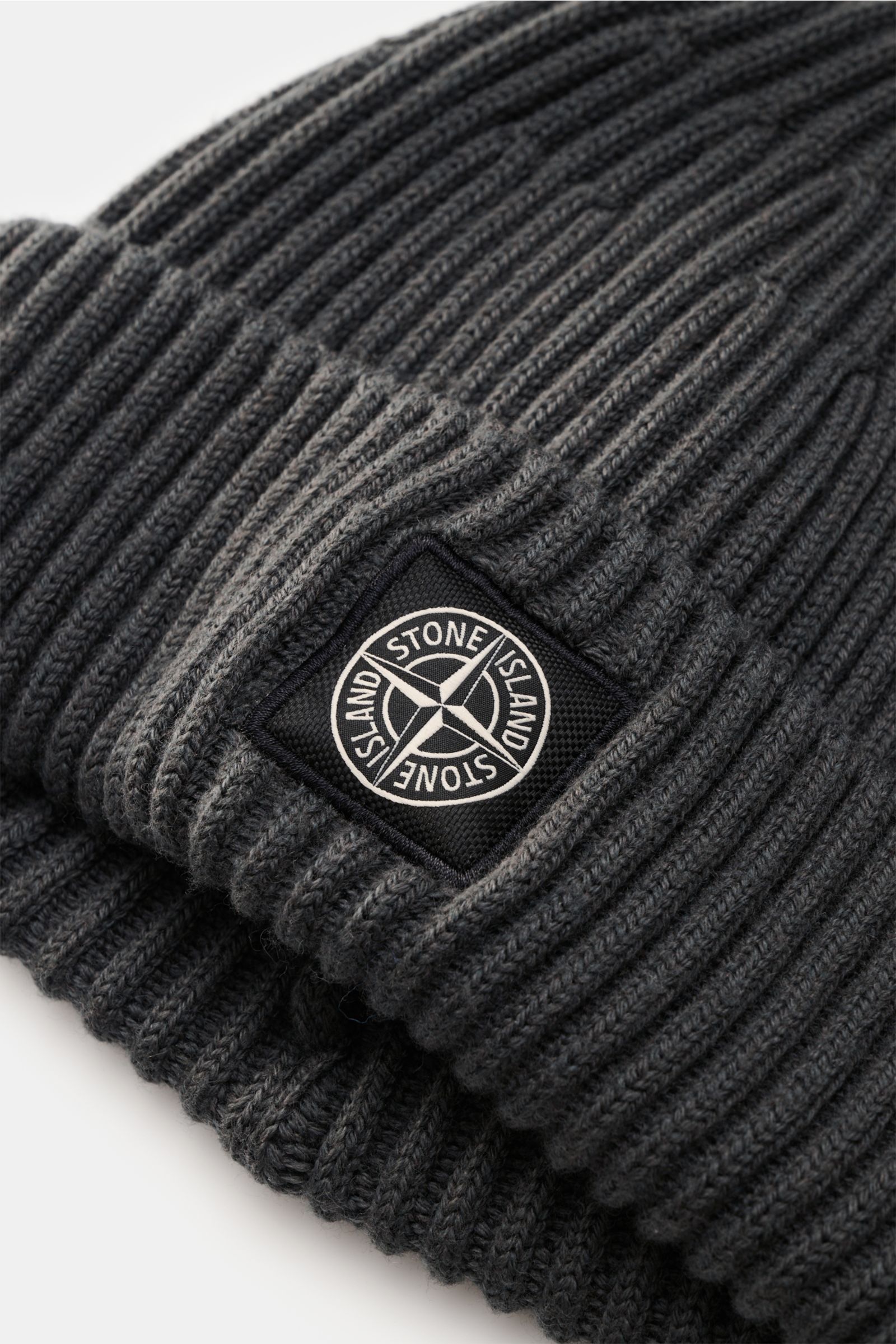 Stone Island Wollmütze dunkelgrau aus reiner Wolle, weicher Griff, moderne Rippstrick-Optik, breiter Umschlag, Front mit STONE ISLAND-Weblabel, Nahaufnahme seitlich.