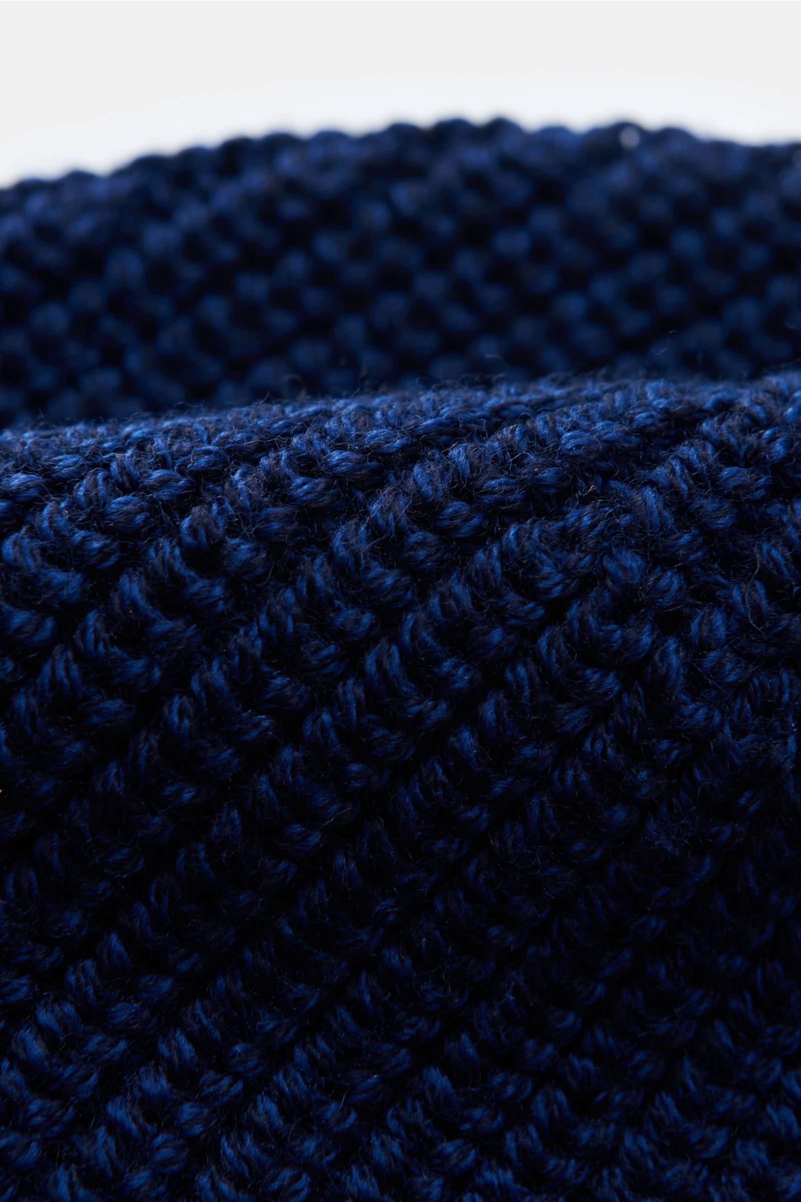 Nahaufnahme der Canada Goose Wollmütze dunkelblau aus reinem Woll-Rippstrick mit grobem Design und Umschlag mit Weblabel, griffige Qualität sichtbar.