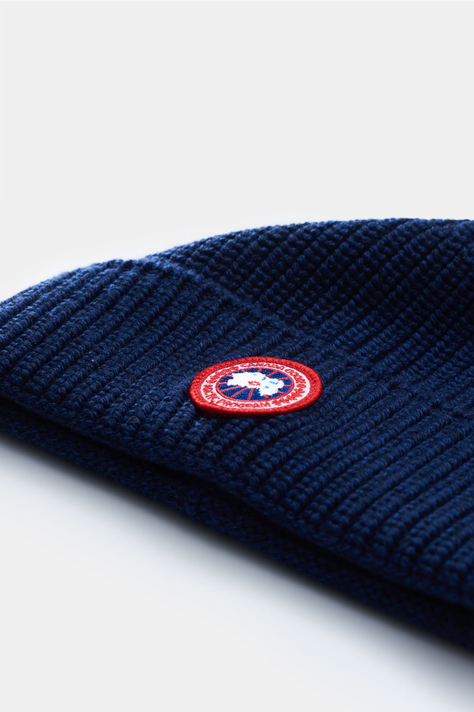 Canada Goose Wollmütze dunkelblau aus reiner Wolle, grobes Rippstrick-Design mit Umschlag und Weblabel, seitliche Nahaufnahme.