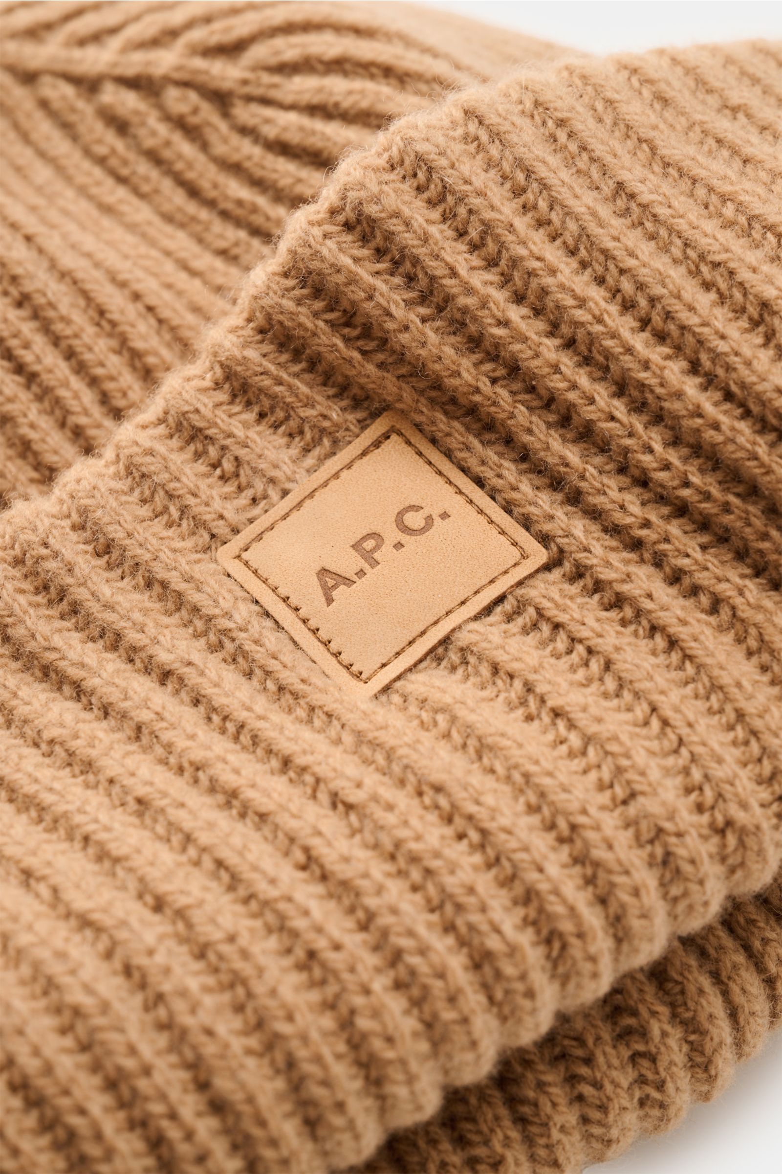 Close-up front view of A.P.C. Wollmütze 'Michelle' hellbraun in heavy rib knit wool and cashmere with wide cuff and stitched logo patch. Französische Coolness für den Winter: Die Wollmütze 'Michelle' von A.P.C. wurde in schwerem Rippstrick aus Wolle und C