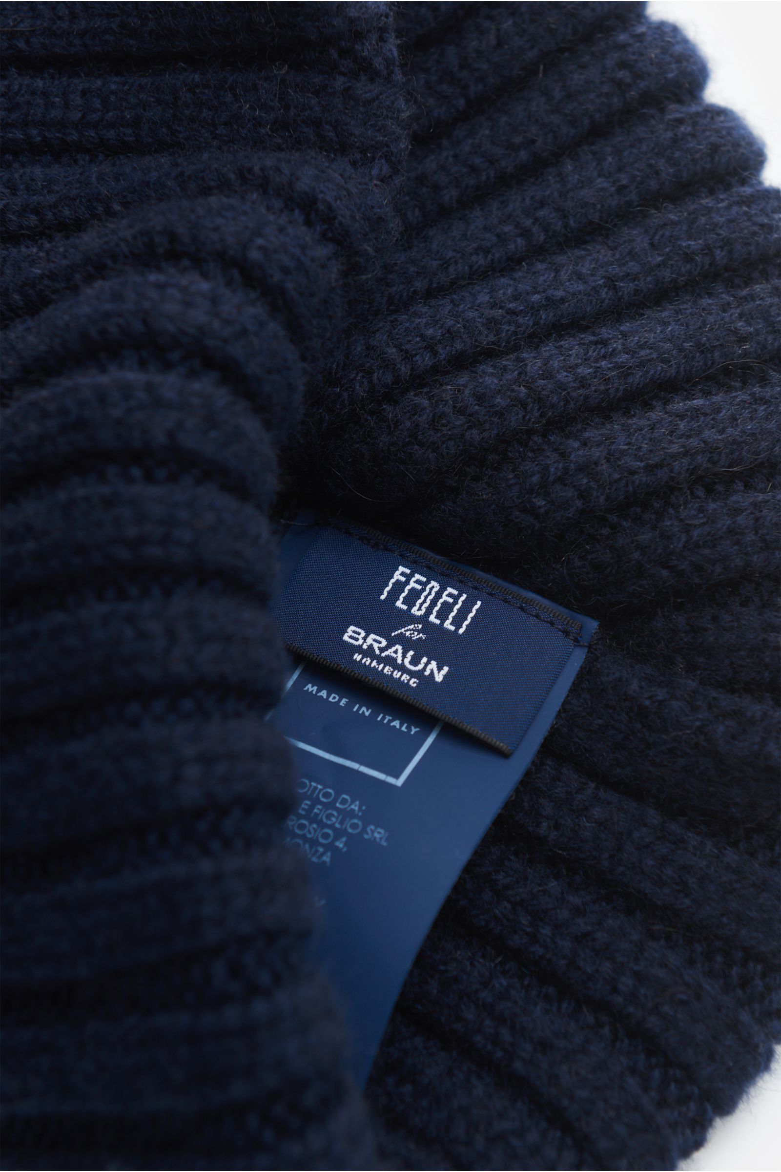 Fedeli Cashmere Mütze navy aus weichem, breitem Rippstrick mit variablem Umschlag, Detailaufnahme des Etiketts von oben fotografiert.
