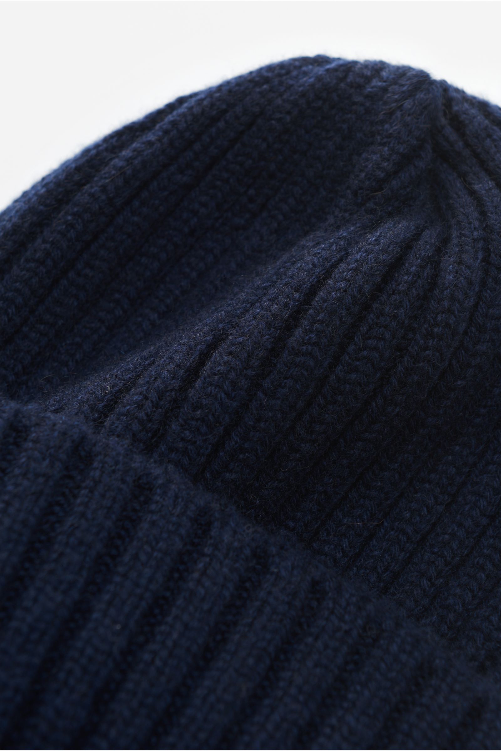 Nahaufnahme der Fedeli Cashmere Mütze navy aus reiner, weicher Cashmere-Faser mit breitem Rippstrick, mittelfeinem Strickbild und variablem Umschlag, fotografiert aus schräger Perspektive.