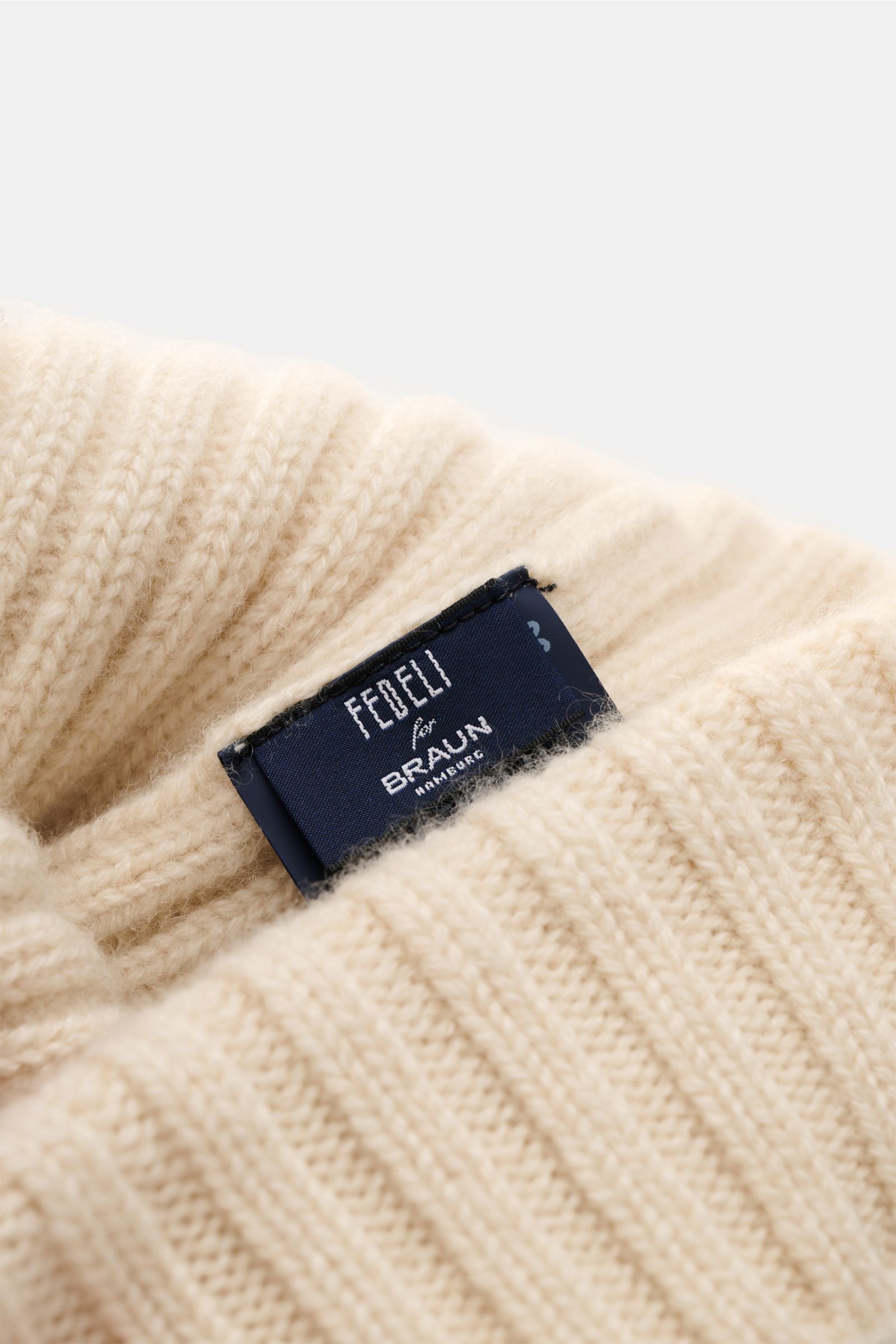 Nahaufnahme der Fedeli Cashmere Mütze creme mit breitem Rippstrick und Label, mittelfeines Strickbild, weicher Griff, variabler Umschlag, reiner Cashmere.