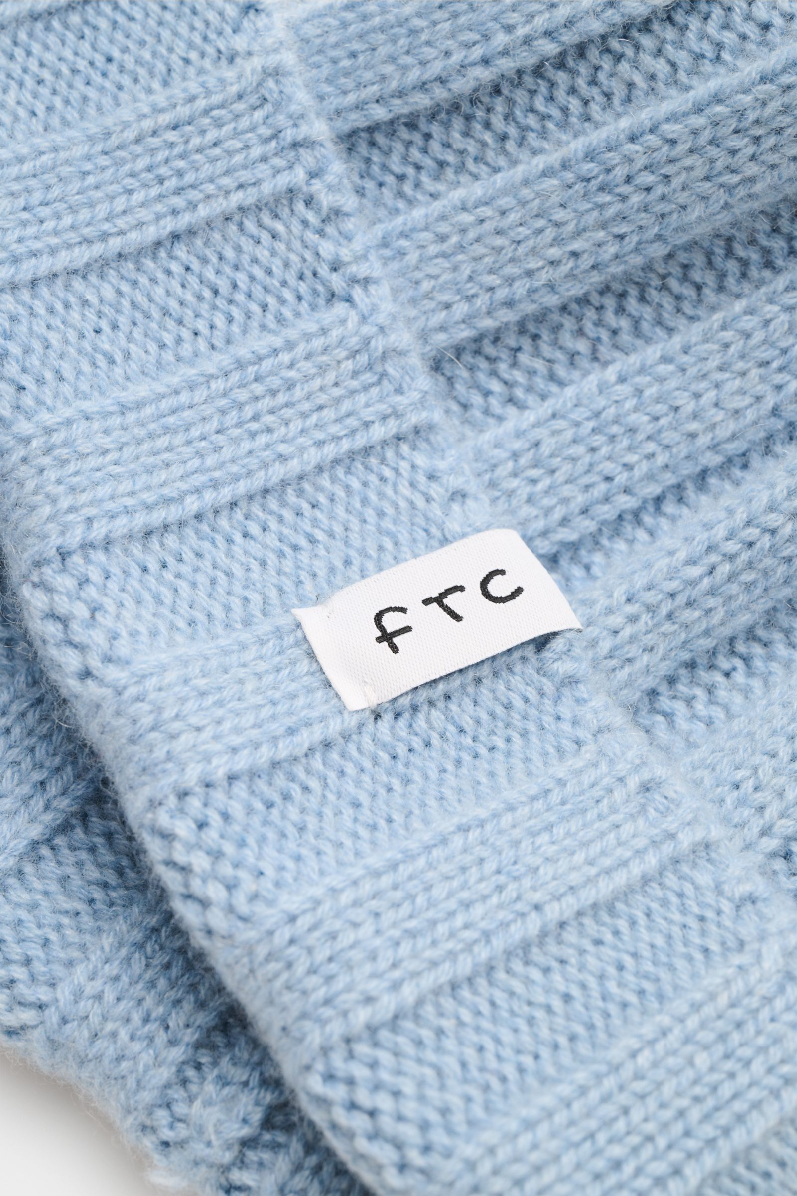 FTC Cashmere Mütze hellblau in Nahaufnahme, Rippstrick mit mittelfeinem Strickbild, schmaler Umschlag mit FTC-Weblabel, weicher Griff aus reinem Fair-Trade-Cashmere.