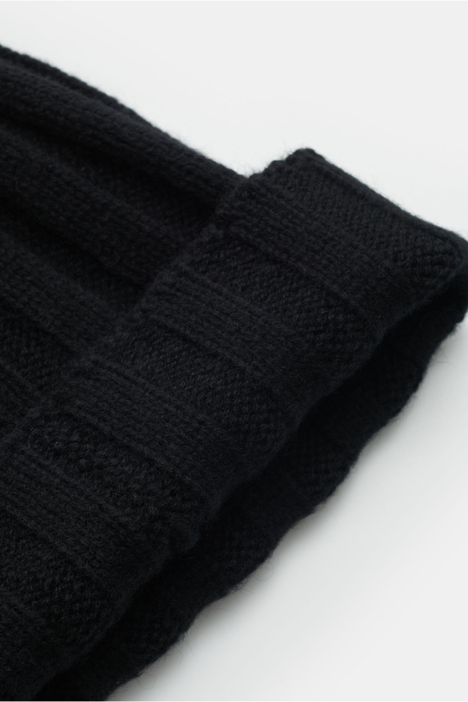 FTC Cashmere Mütze schwarz, Detailaufnahme seitlich von oben, feiner Fair-Trade Cashmere-Rippstrick, weicher Griff, schmaler Umschlag mit FTC-Weblabel.