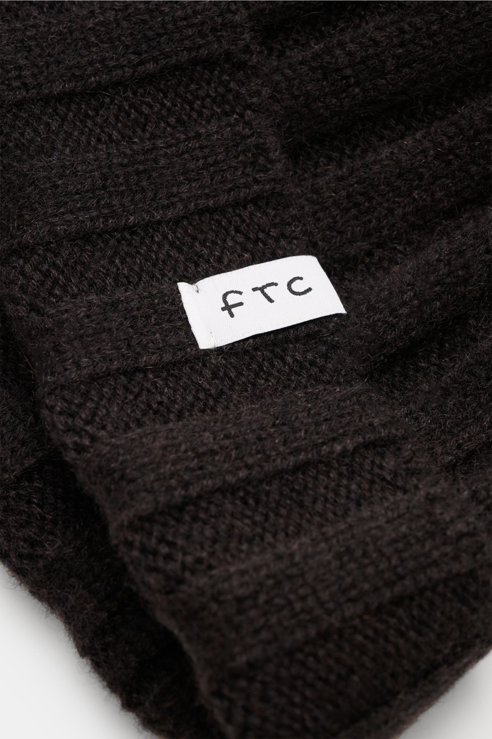 Nahaufnahme der FTC Cashmere Mütze dunkelbraun aus feinstem Fair-Trade-Cashmere mit weichem Griff, Rippstrickmuster, mittelfeinem Strickbild und schmalem Umschlag mit FTC-Weblabel.