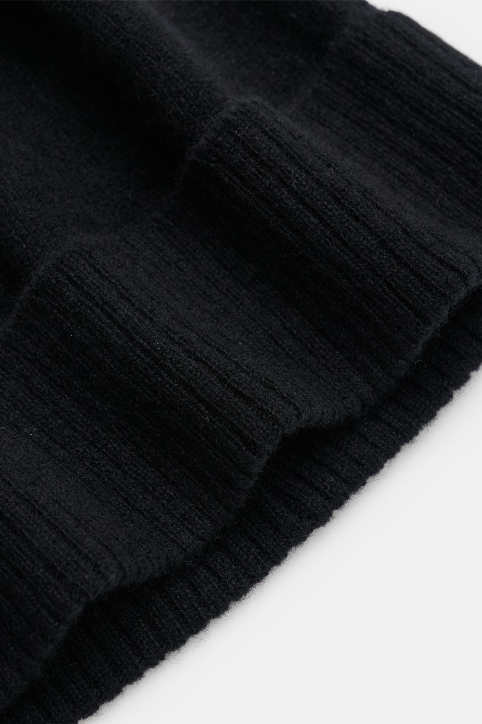 Schräg von oben fotografierte 04651/ A trip in a bag Cashmere Mütze schwarz mit feinem Strickbild, weichem Griff und Rippstrick-Umschlag.