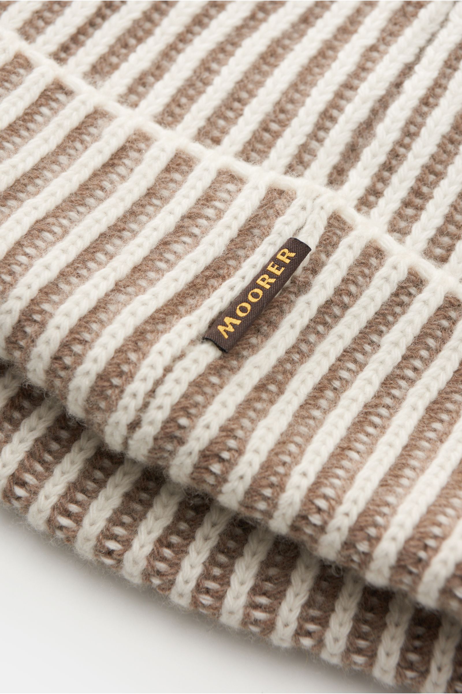 Close-up angled view of the Moorer Beanie 'Davis-WSV' white/taupe striped showing a blend of wool and cashmere, very soft feel, two-tone brioche pattern, chunky knit, and a small woven label in the seam.