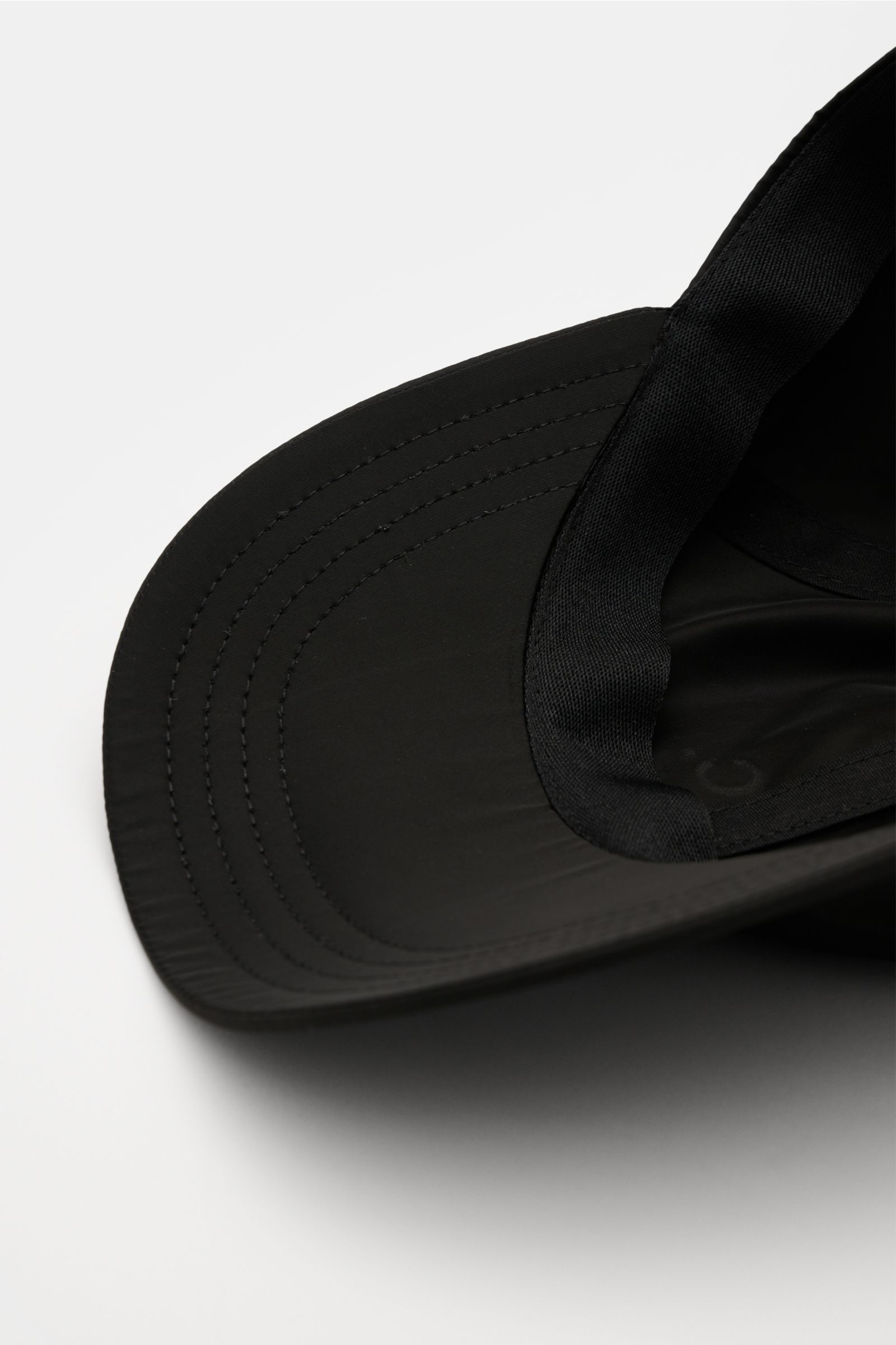 A close-up, inside view of the black A.P.C. Baseball-Cap 'Charlie' schwarz showing the curved brim and inner stitching, made of lightweight microfiber with a clean six-panel design, logo print on the front, and an adjustable strap. Lässiger Urban Style