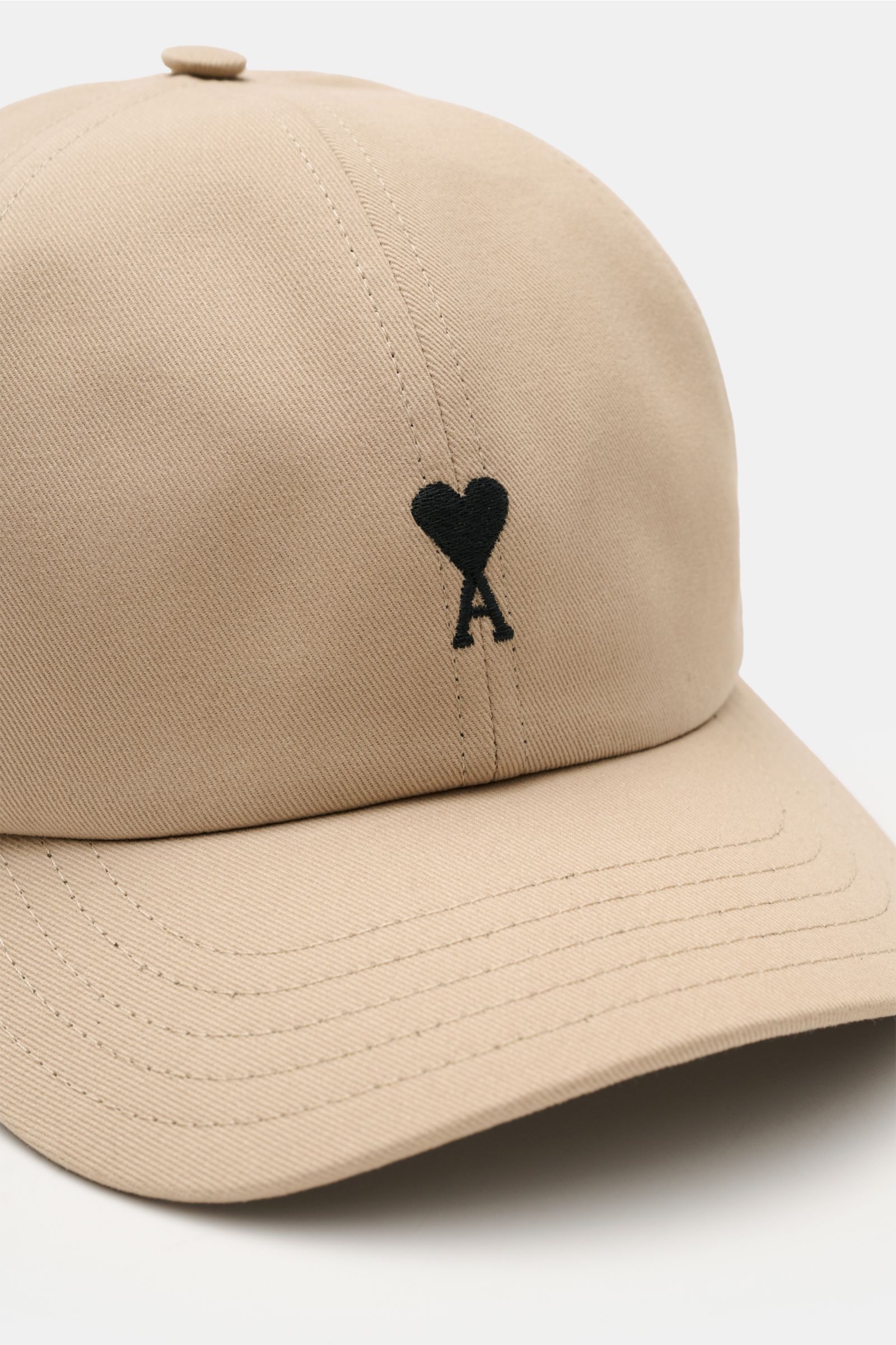 Ami Paris Baseball-Cap beige aus reiner Baumwolle mit weichem Griff, gebogenem Schirm, verstellbarem Verschluss und schwarzem Herz-Logo, Nahaufnahme frontseitig.