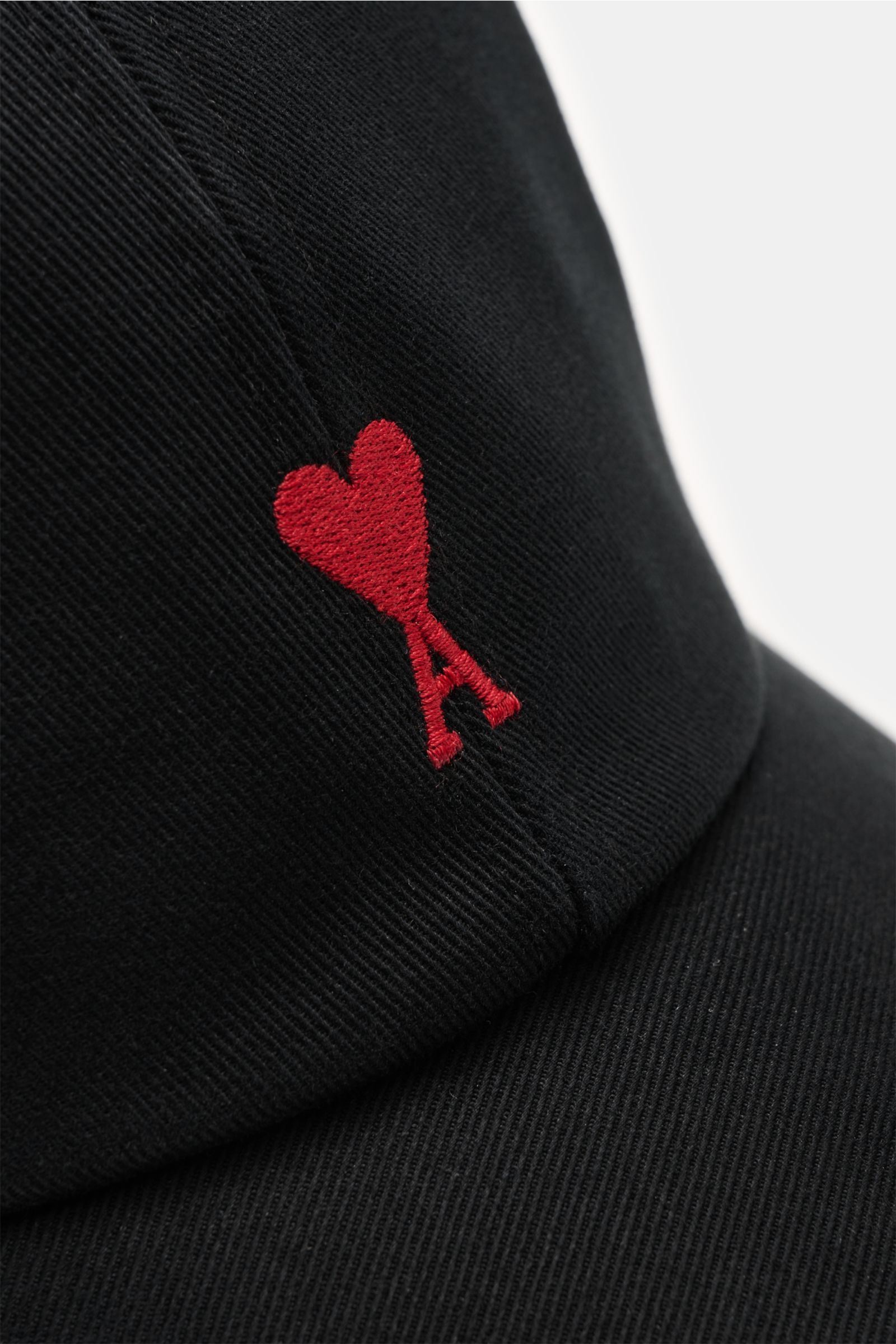 Ami Paris Baseball-Cap schwarz shown from a close-up front angle, made of pure cotton with a soft feel, curved brim, and red heart logo embroidery. A french affair: Diese Baseball-Cap aus reiner Baumwolle von AMI PARIS ergänzt Ihren Look stilvoll und w