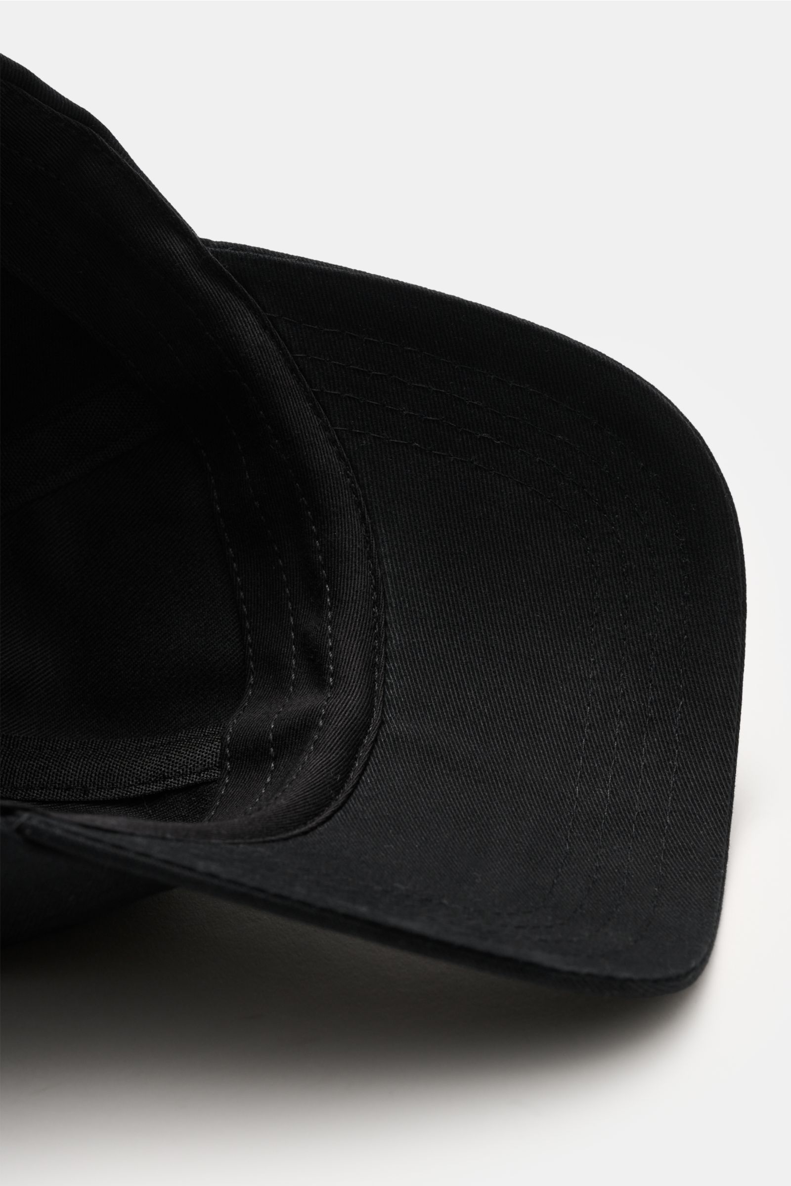 A close-up, angled view of the Ami Paris Baseball-Cap schwarz showing the black cotton fabric and curved brim with detailed stitching. A french affair: Diese Baseball-Cap aus reiner Baumwolle von AMI PARIS ergänzt Ihren Look stilvoll und wird von dem typi