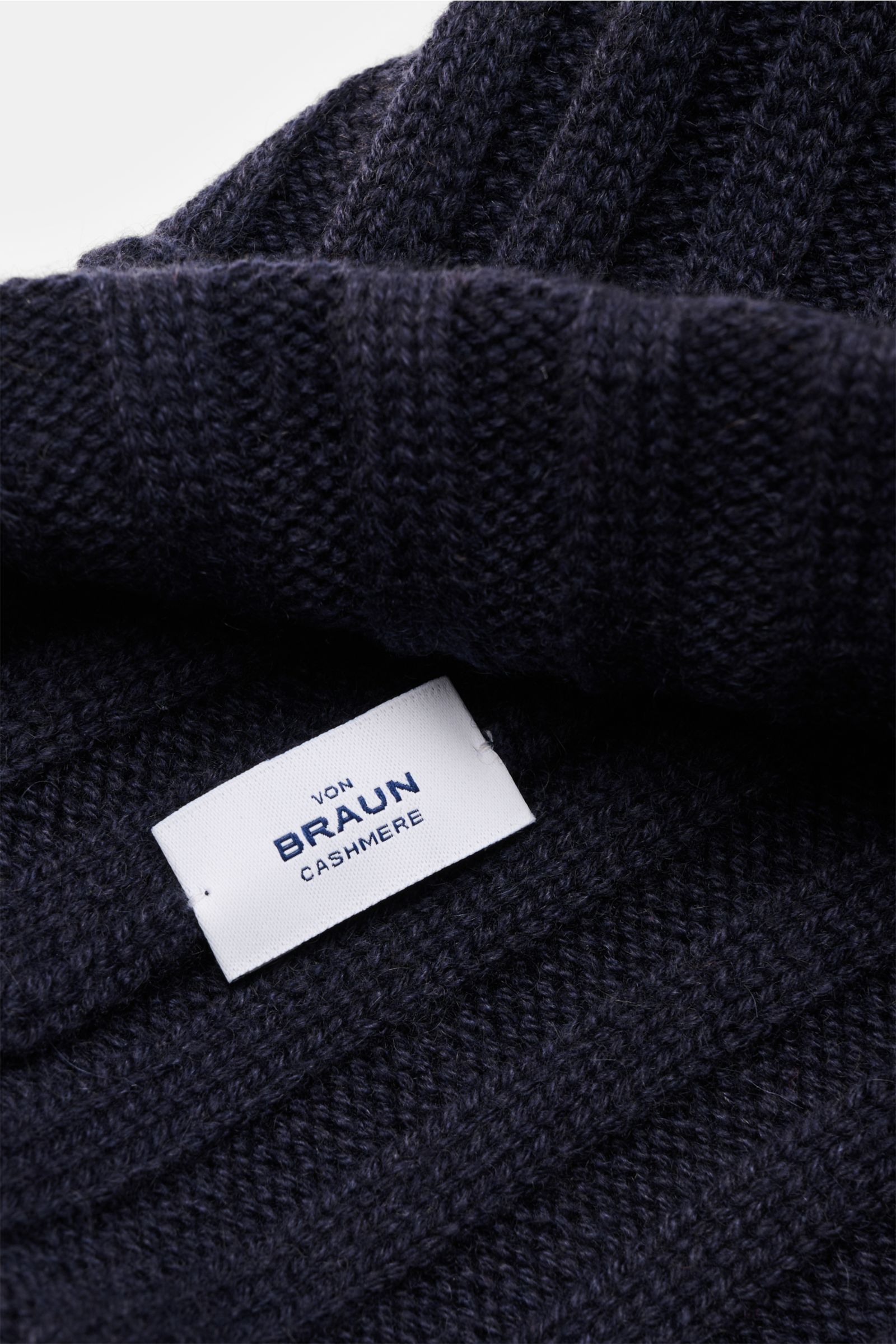 Nahaufnahme der von Braun Cashmere Mütze navy mit schmalem Umschlag, feinem Rippstrickmuster, weichem Griff aus reinem mongolischem Cashmere, fotografiert von schräger Seite.
