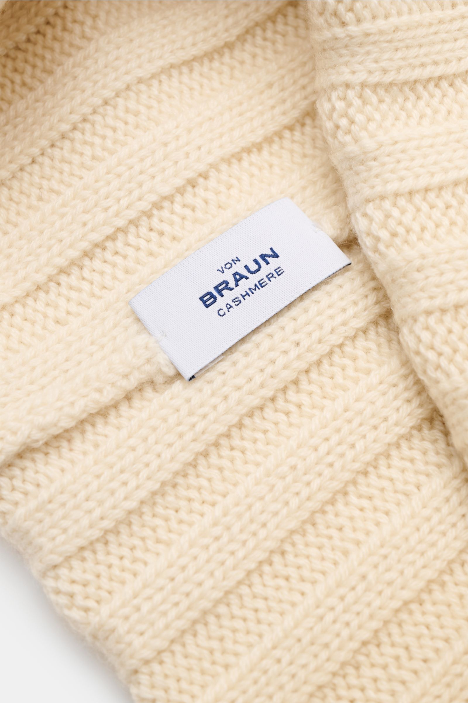 Nahaufnahme der von Braun Cashmere Mütze offwhite aus reinem mongolischem Cashmere mit feinem, weichem Rippstrickmuster und schmalem Umschlag, seitlich fotografiert.