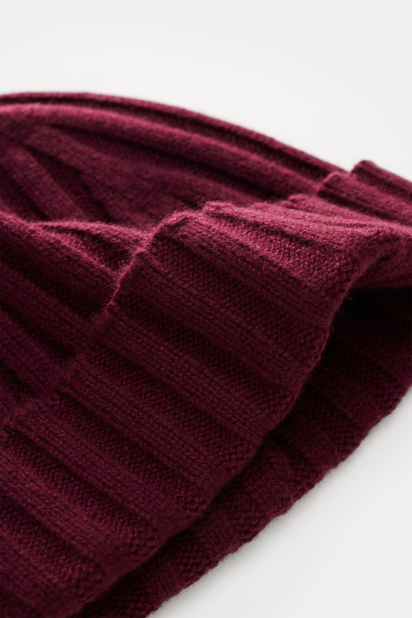 Nahaufnahme der von Braun Cashmere Mütze bordeaux aus reinem mongolischem Cashmere, schmaler Umschlag, feines Rippstrickmuster, sehr weich, aus schräger Perspektive.