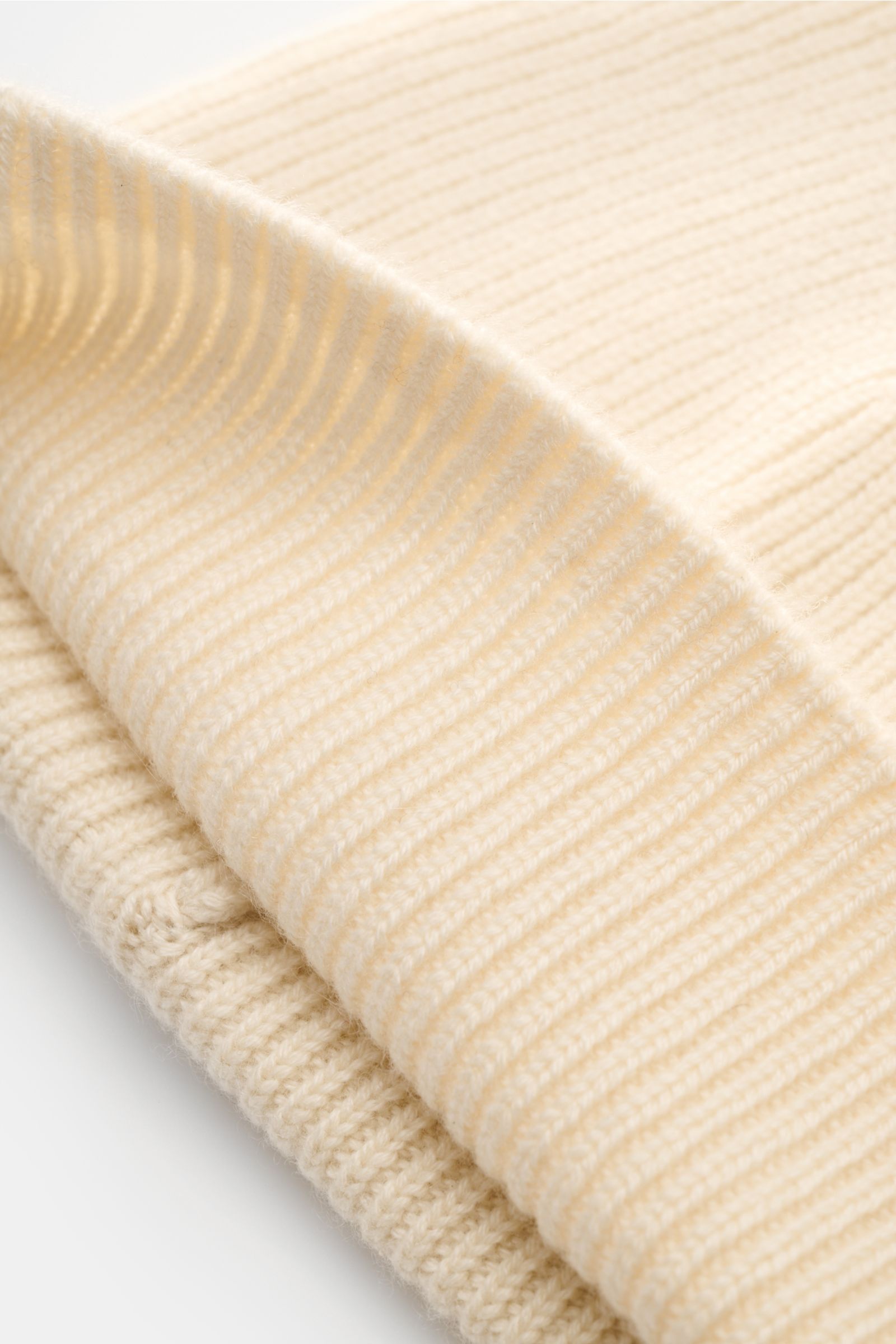 Close-up side view of the von Braun Cashmere beanie off-white showing its fine classic brioche knit pattern and small turn-up cuff, made of pure cashmere with a soft feel, an essential winter accessory. Wear it with a classic winter coat or high function 