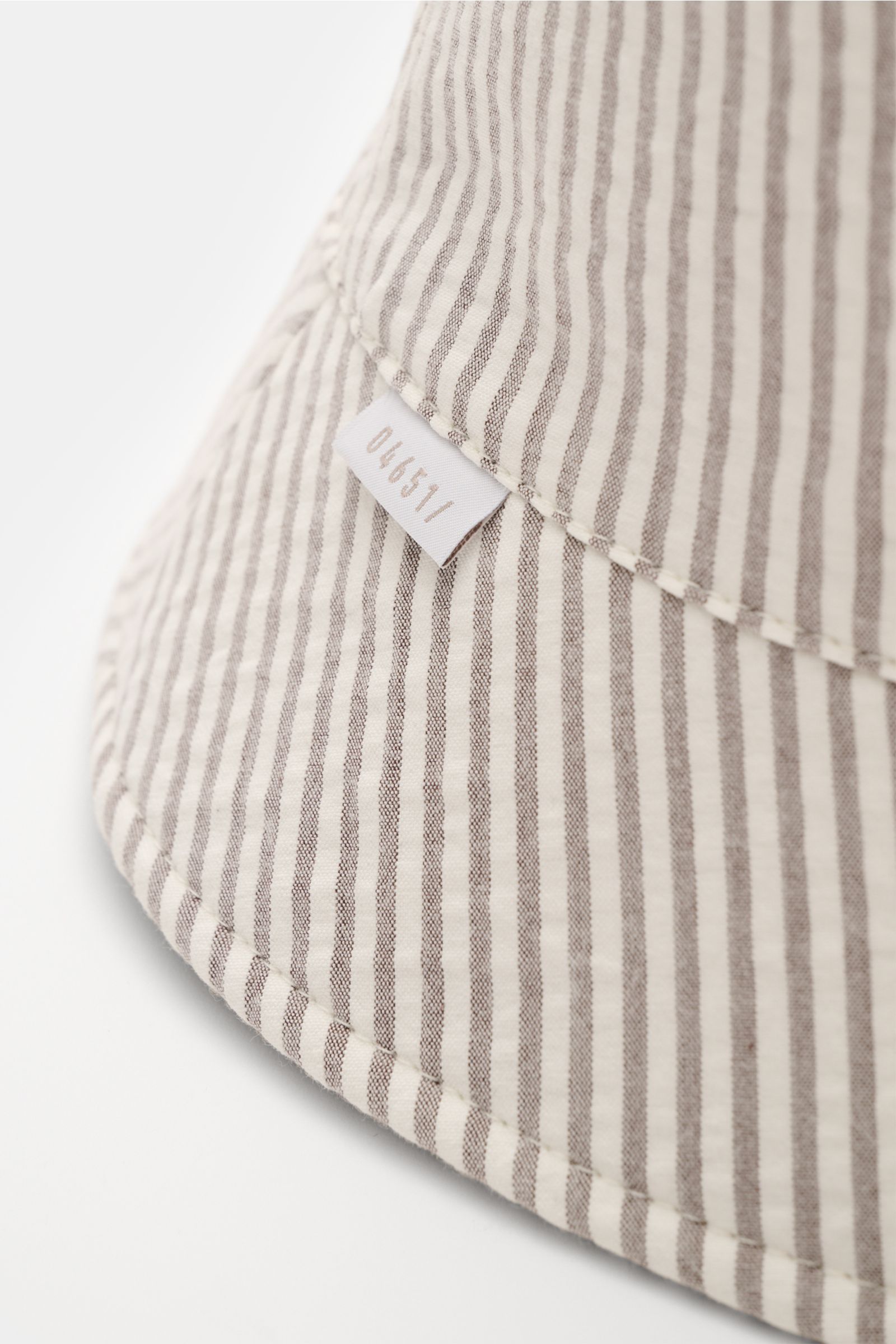 Close-up front-side view of the 04651/ A trip in a bag Wende-Frottee Bucket Hat beige featuring beige and white striped seersucker fabric, small logo tag, soft cotton terry texture, narrow brim, and reversible design. Vielseitiger Urlaubsbegleiter: Der Bu