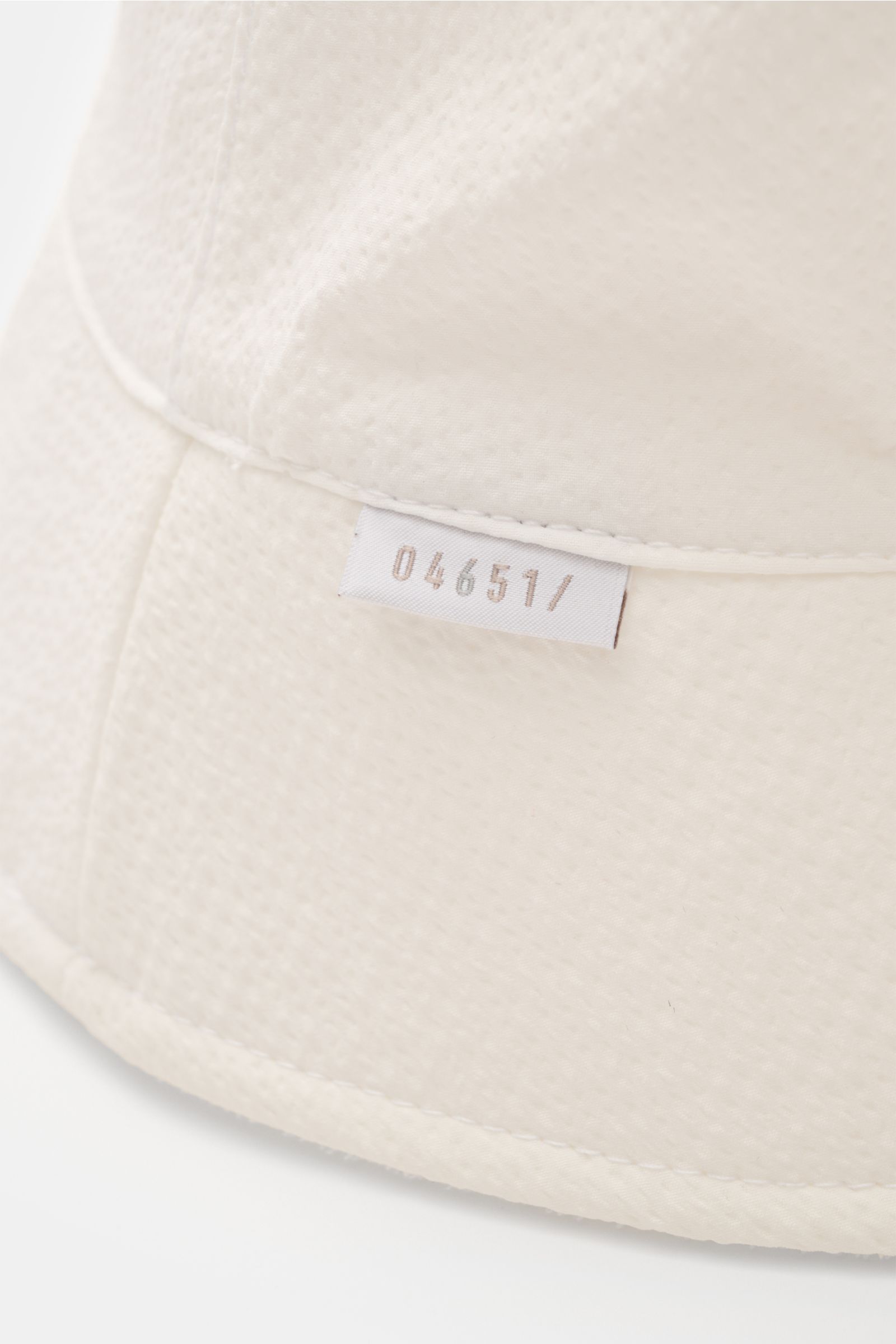Close-up front-side view of the 04651/ A trip in a bag Wende-Frottee Bucket Hat weiß, showing its textured elastic cotton terry fabric, small A TRIP IN A BAG label, and soft, narrow brim. Vielseitiger Urlaubsbegleiter: Der Bucket Hat von 04651/ A TRIP IN 
