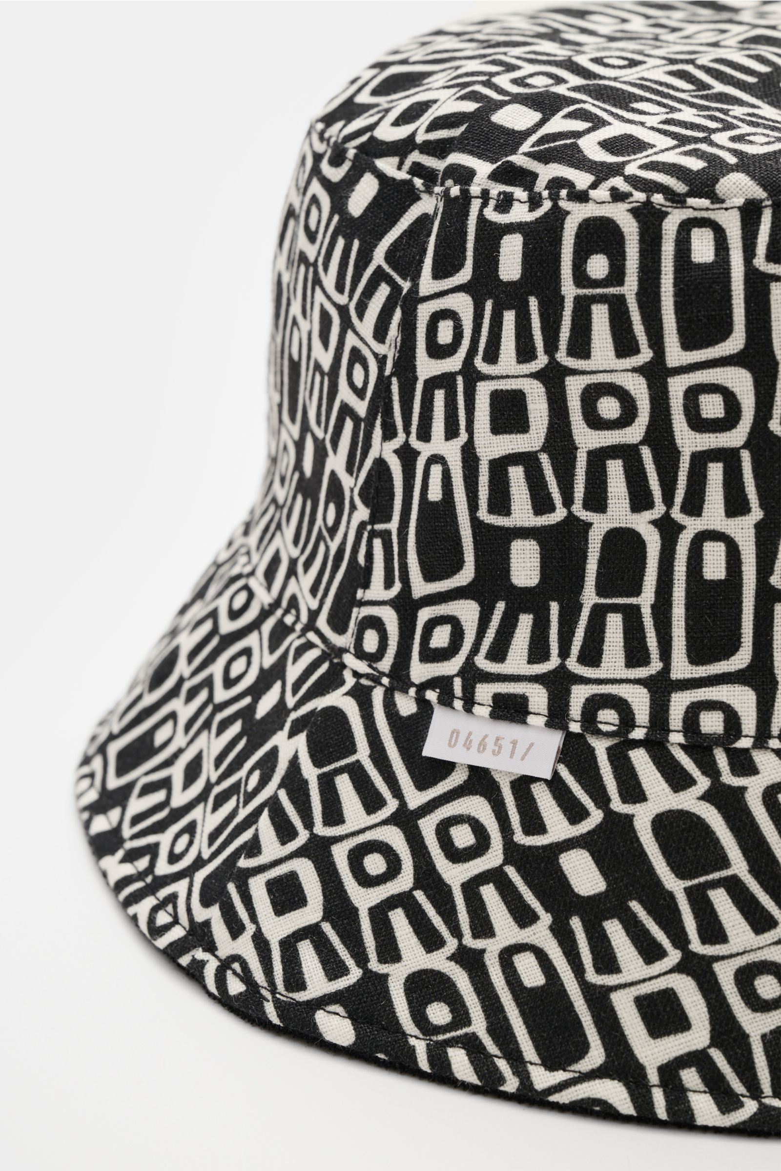 04651/ A trip in a bag Wende-Frottee Bucket Hat schwarz, elastischer Baumwoll-Frottee mit gemustertem Innenfutter, wendbar, schmale Krempe, weiche Haptik, kleines Weblabel, Nahaufnahme von schräg oben.