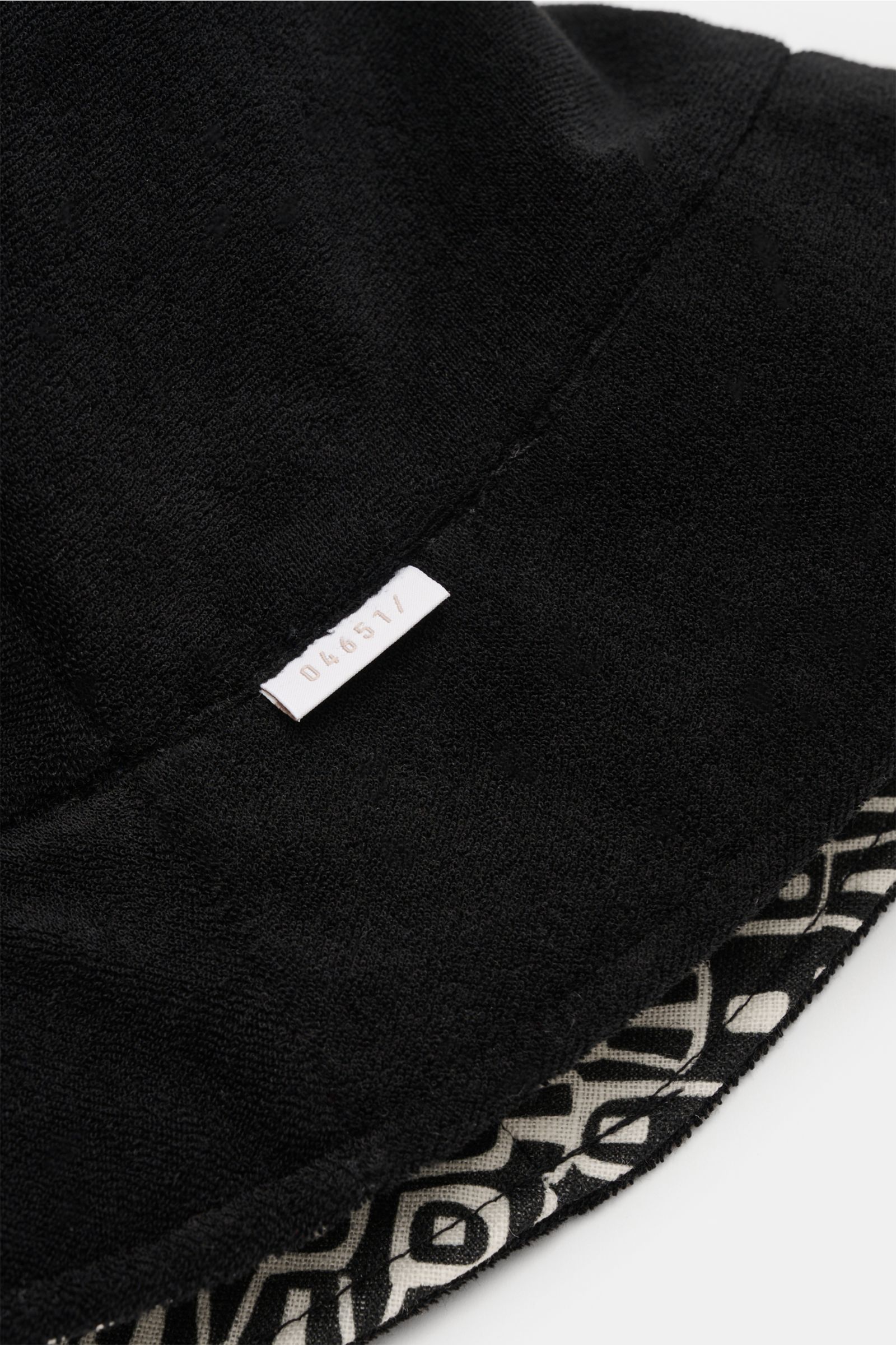 04651/ A trip in a bag Wende-Frottee Bucket Hat schwarz, Detailaufnahme von oben, elastischer Baumwollfrottee mit gemustertem Innenfutter, schmale Krempe, weiches Material, kleines Weblabel sichtbar.