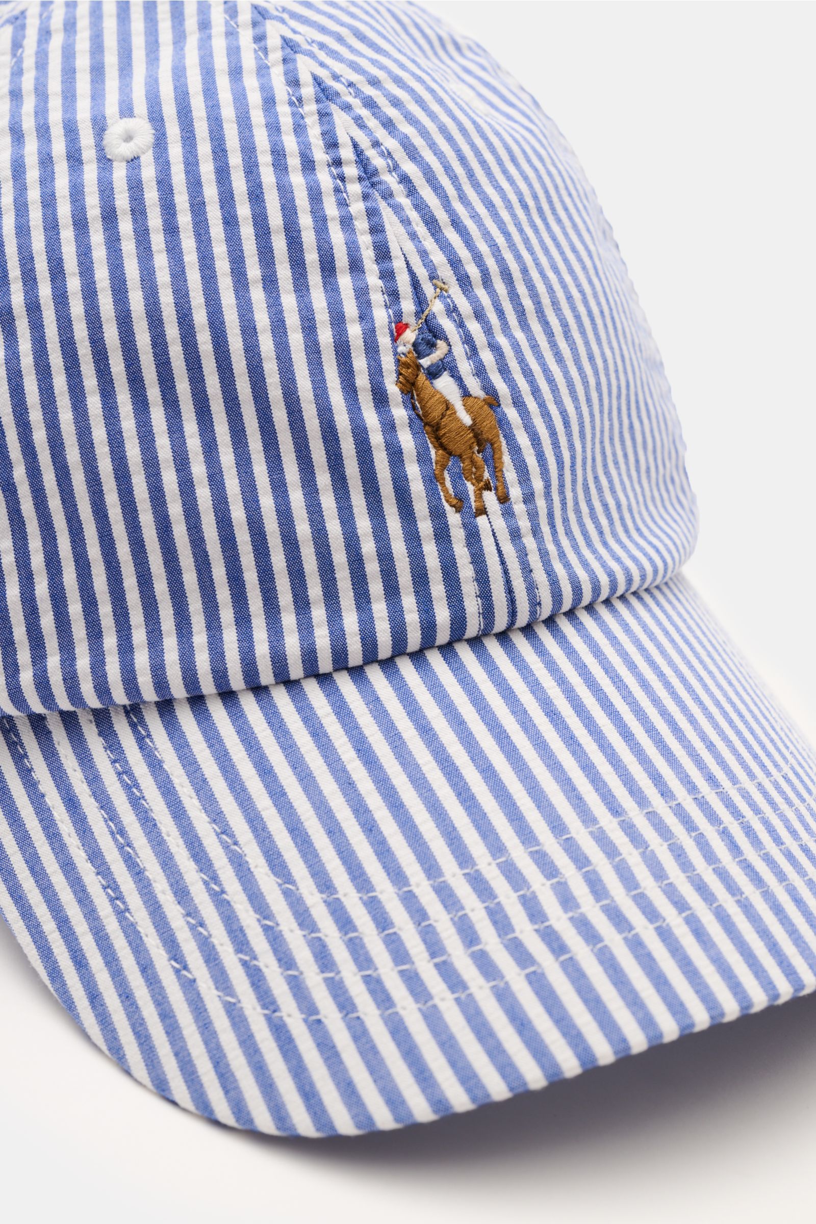 Nahaufnahme einer Polo Ralph Lauren Baseball-Cap blau/weiß gestreift aus Baumwolle mit sechs-Panel-Design, gebogenem Schirm, Logo-Stitching und verstellbarem Verschluss, fotografiert von schräg oben.