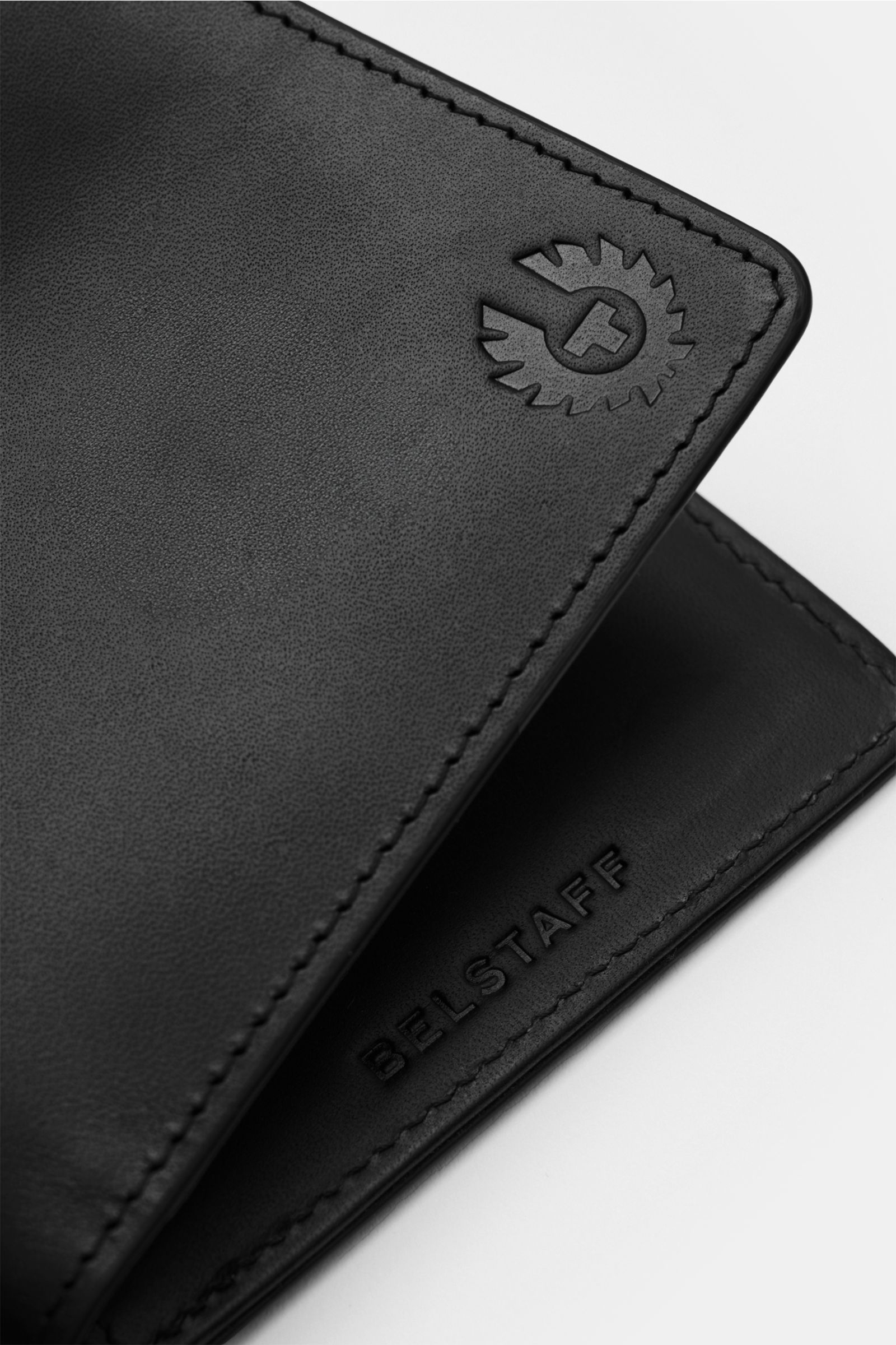 Close-up, angled view of the Belstaff Portemonnaie schwarz wallet showing smooth black cowhide leather with tonal logo embossing on front and BELSTAFF embossing inside. Der perfekte Alltagsbegleiter: Minimalistische Ästhetik und glattes Leder machen di
