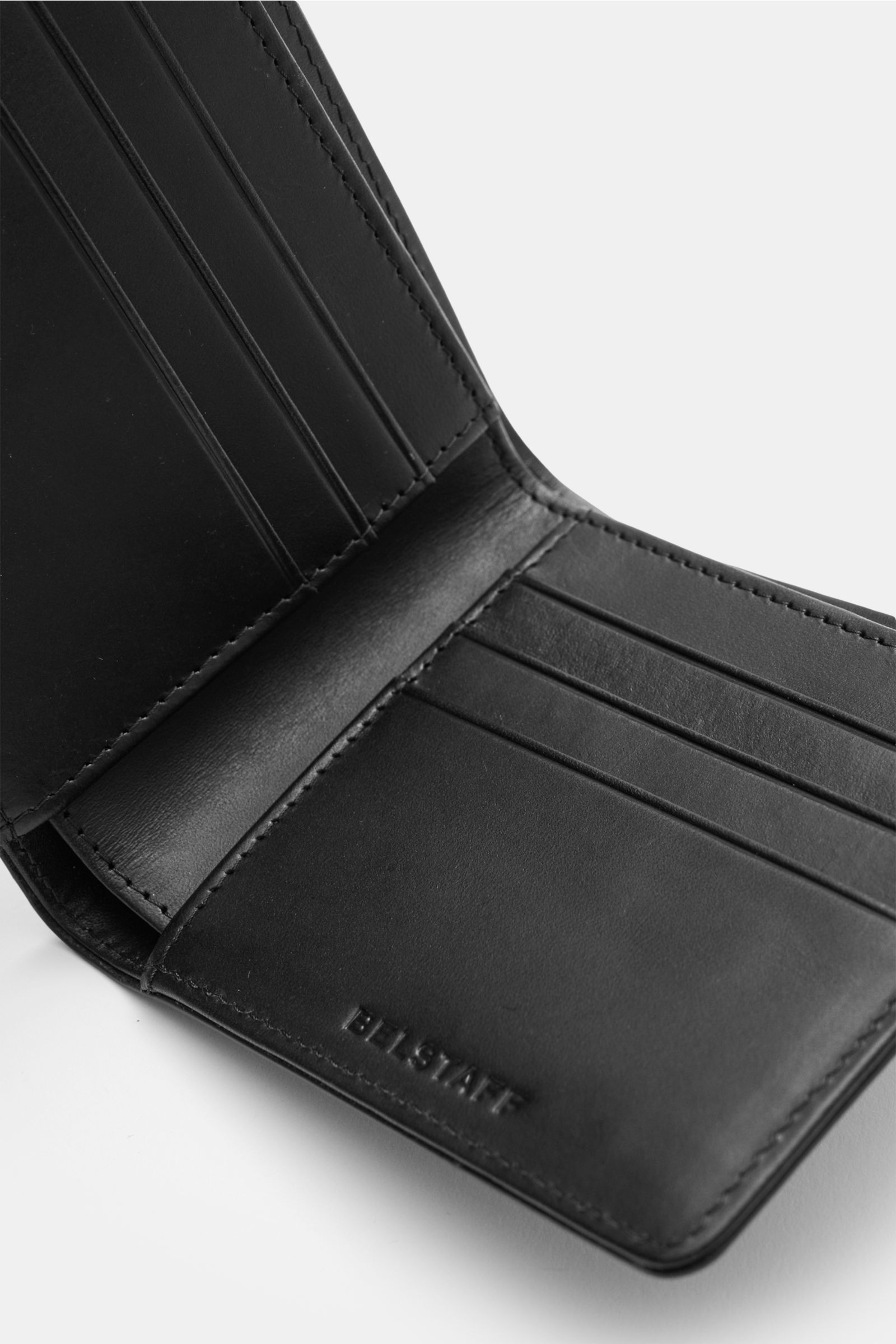 Close-up angled view of the Belstaff Portemonnaie schwarz, a minimalist black leather wallet with tonal logo embossing, smooth cowhide, one banknote compartment, and eight card slots; dimensions approx. 11.5 x 9.5 x 2 cm when closed. Der perfekte Allta