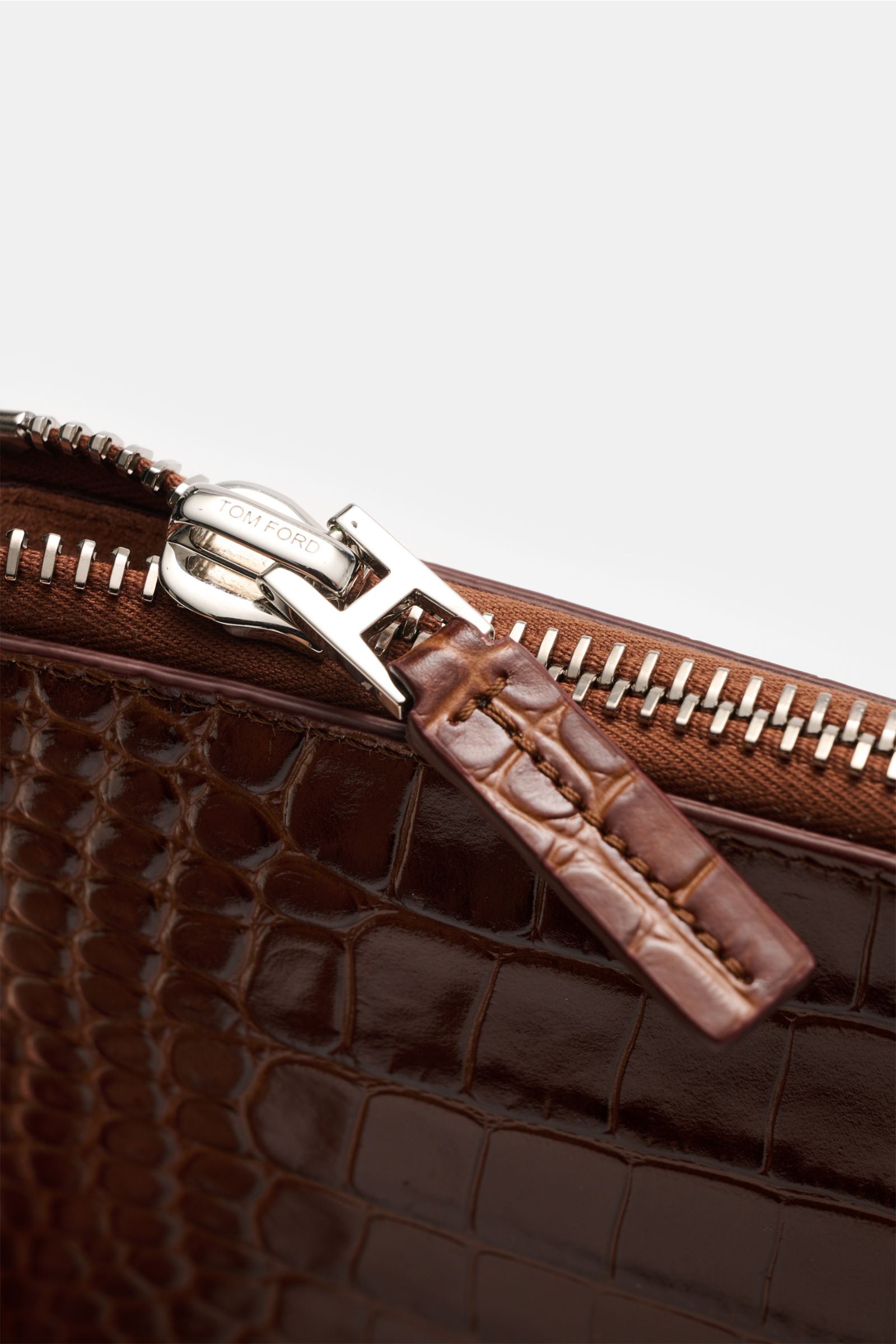 Close-up view of the zipper and reptile-look calf leather texture on the brown Tom Ford Tasche braun, highlighting silver brass hardware.

Praktischer Begleiter im Alltag: Hochwertiges Kalbleder im Reptilien-Look und dezente Logo-Prägung machen diese e