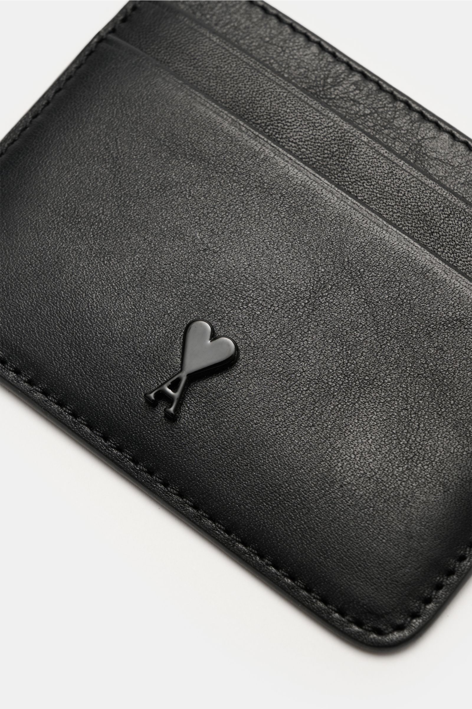 Close-up, angled view of the Ami Paris Kartenetui schwarz made of finely grained black calf leather, featuring a front logo, one central compartment, and four card slots, measuring approximately 10 cm x 8 cm. Stilvolles Accessoire für den Alltag: Diese