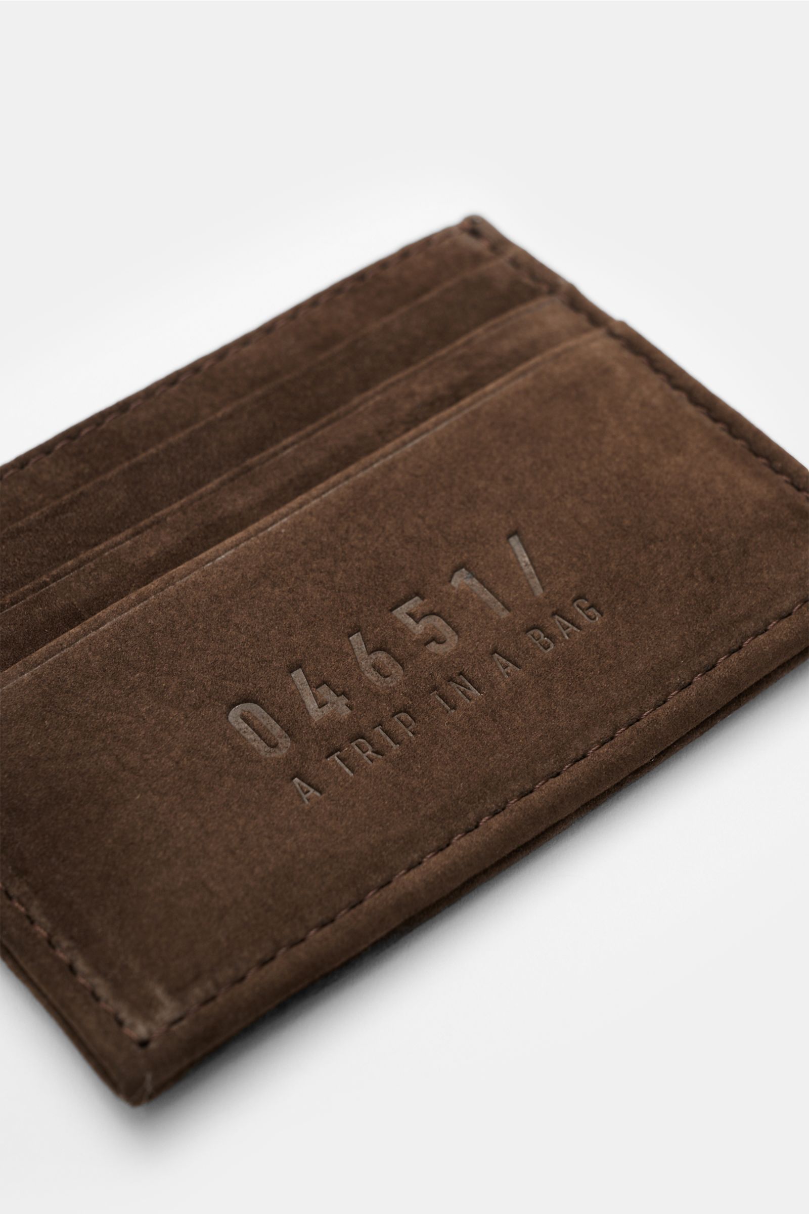 Close-up, angled top view of the 04651/ A trip in a bag Kartenetui dunkelbraun, a flat cardholder in dark brown velour leather with six card slots, main compartment, and embossed 04651/ branding, approx. 10 x 8 cm.

Minimalistisches Alltags-Essential: 