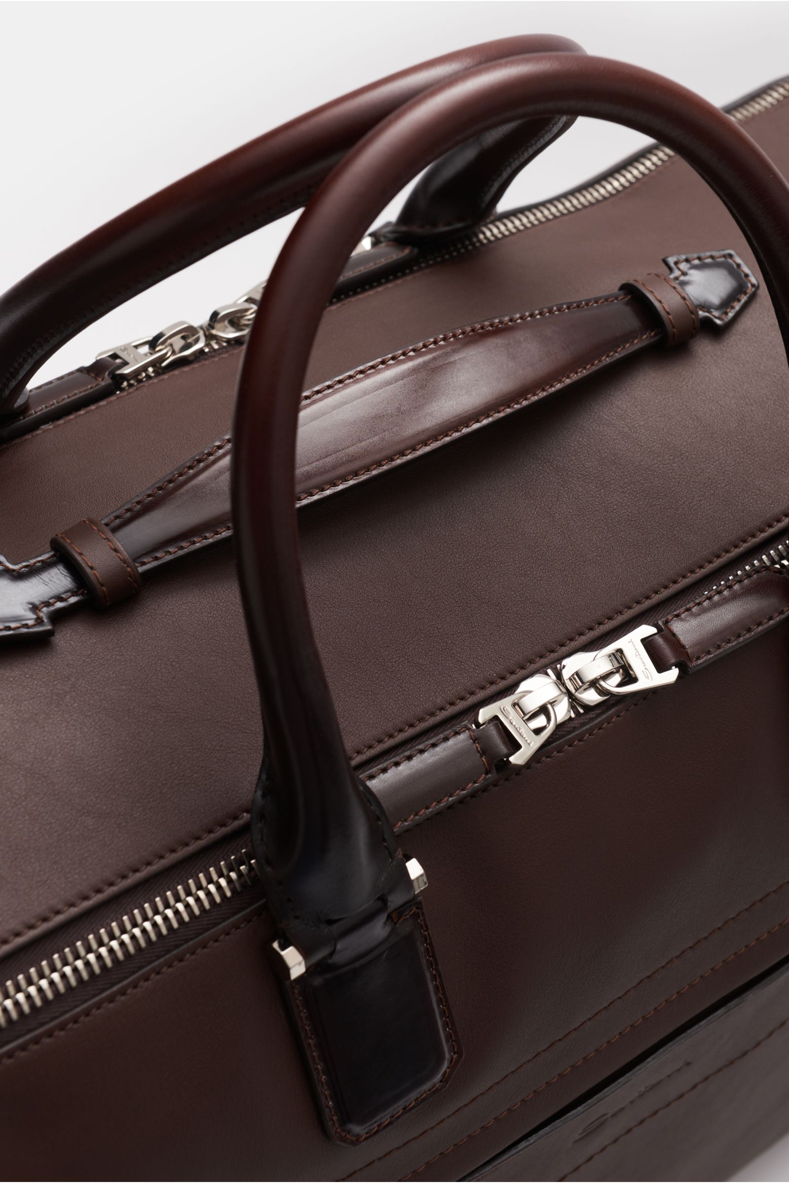 Santoni Weekender braun aus softem, fein genarbtem Glattleder, Nahaufnahme von oben auf robuste Tragegriffe, silberfarbene Hardware und Reißverschluss.