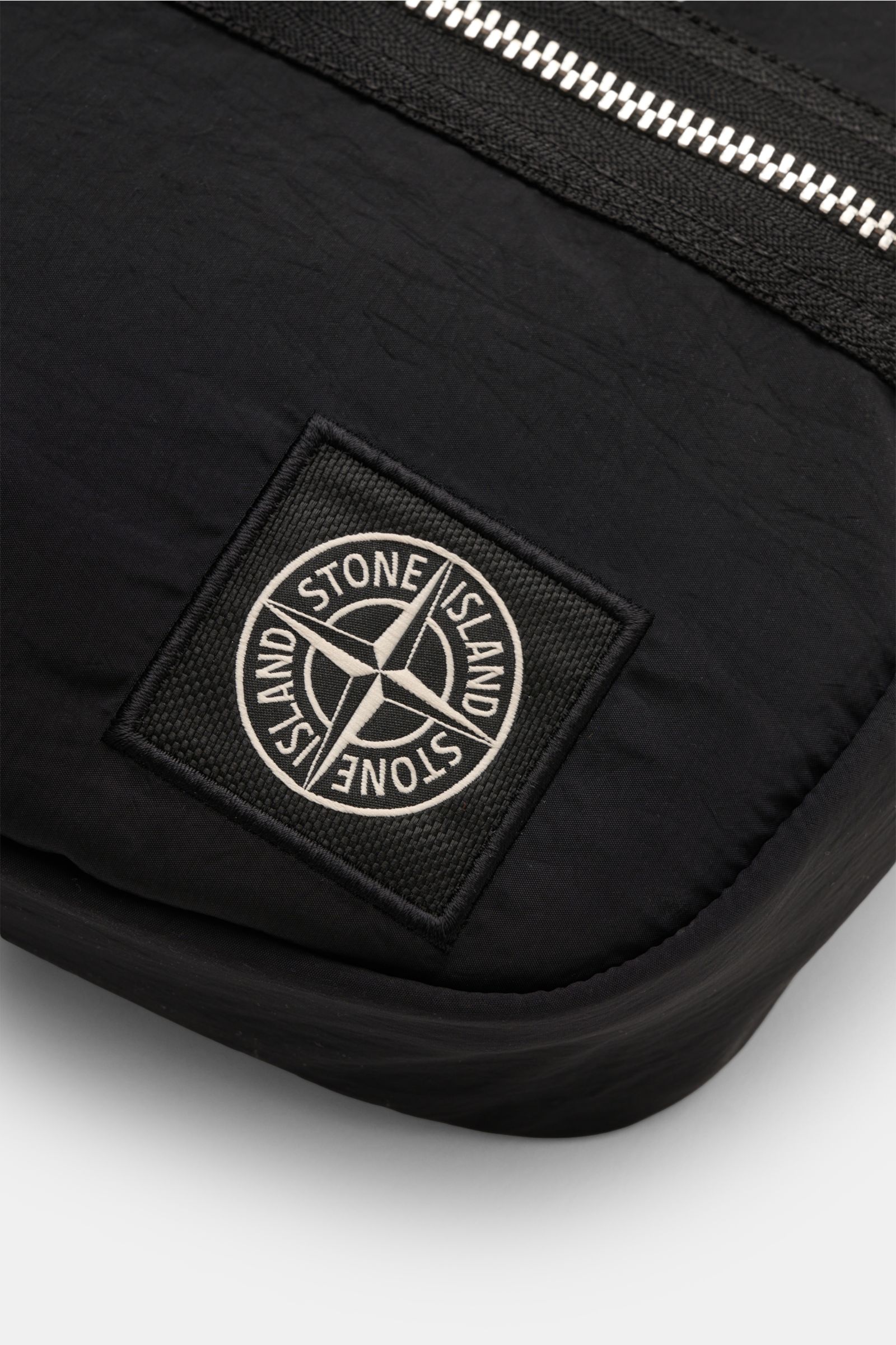 Close-up front view of the Stone Island Gürteltasche schwarz, a minimalist black nylon belt bag with silver zipper, durable strap, and signature Windrose patch.  

Praktisches Accessoire von STONE ISLAND: In dieser minimalistischen Gürteltasche aus ang