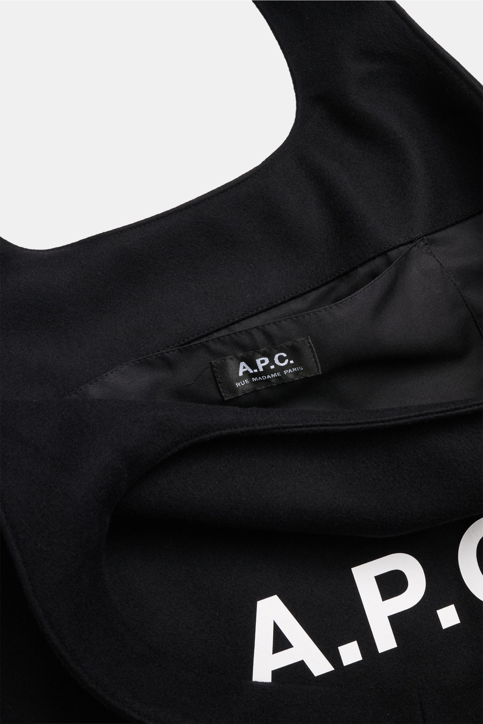 Close-up view of the interior and front logo of A.P.C. Shopper 'Ninon' schwarz, showing mix of wool, microfiber, and cashmere, wide handles, spacious main compartment, one slip pocket, front with logo print, dimensions approx. 48 cm x 36 cm x 17 cm.