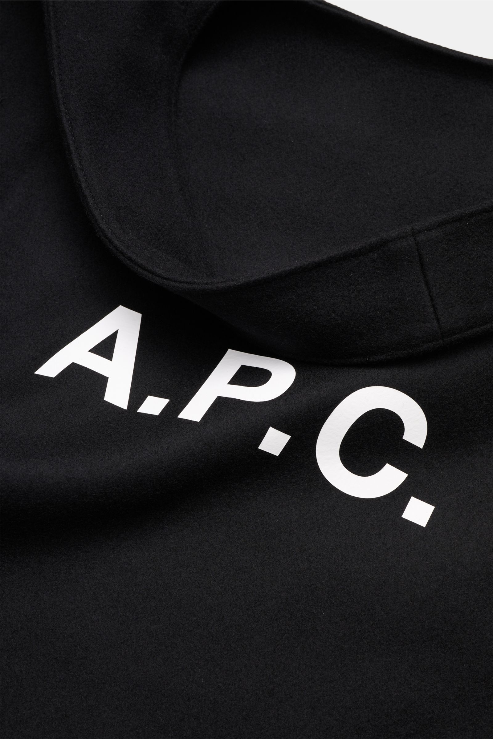 Close-up photo of the black A.P.C. Shopper 'Ninon' schwarz showing the front logo print and part of the wide handle. Mix aus Wolle, Microfaser und Cashmere, breite Henkel, geräumiges Hauptfach, ein Steckfach, Front mit Logo-Print, Maße: ca. 48 cm x 36 cm 