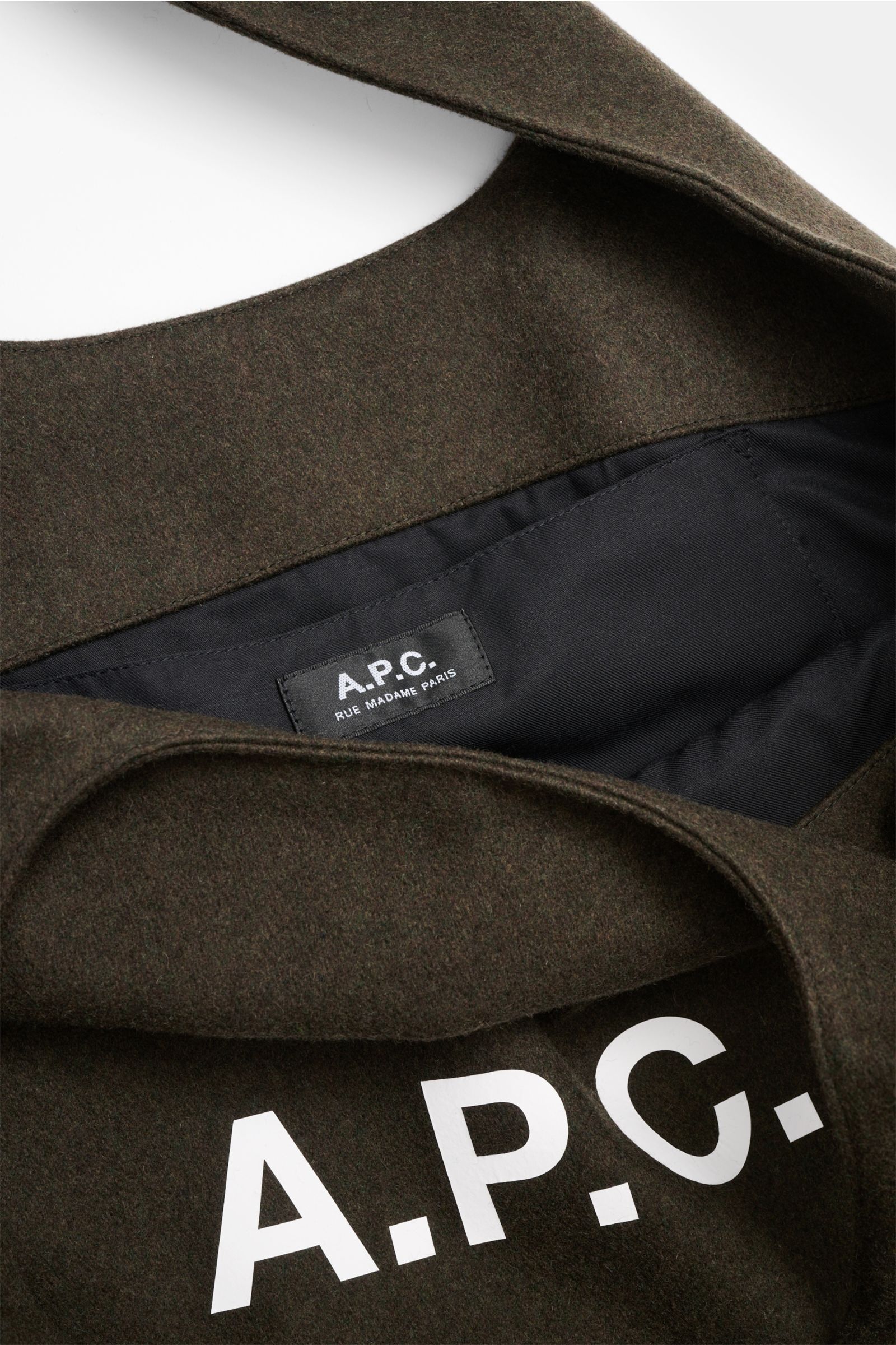 Nahaufnahme aus schräger Perspektive des A.P.C. Shopper 'Ninon' dark olive mit breiten Henkeln, Logo-Print, Innenfutter, Steckfach, Mix aus Wolle, Microfaser, Cashmere, Maße ca. 48x36x17 cm.
