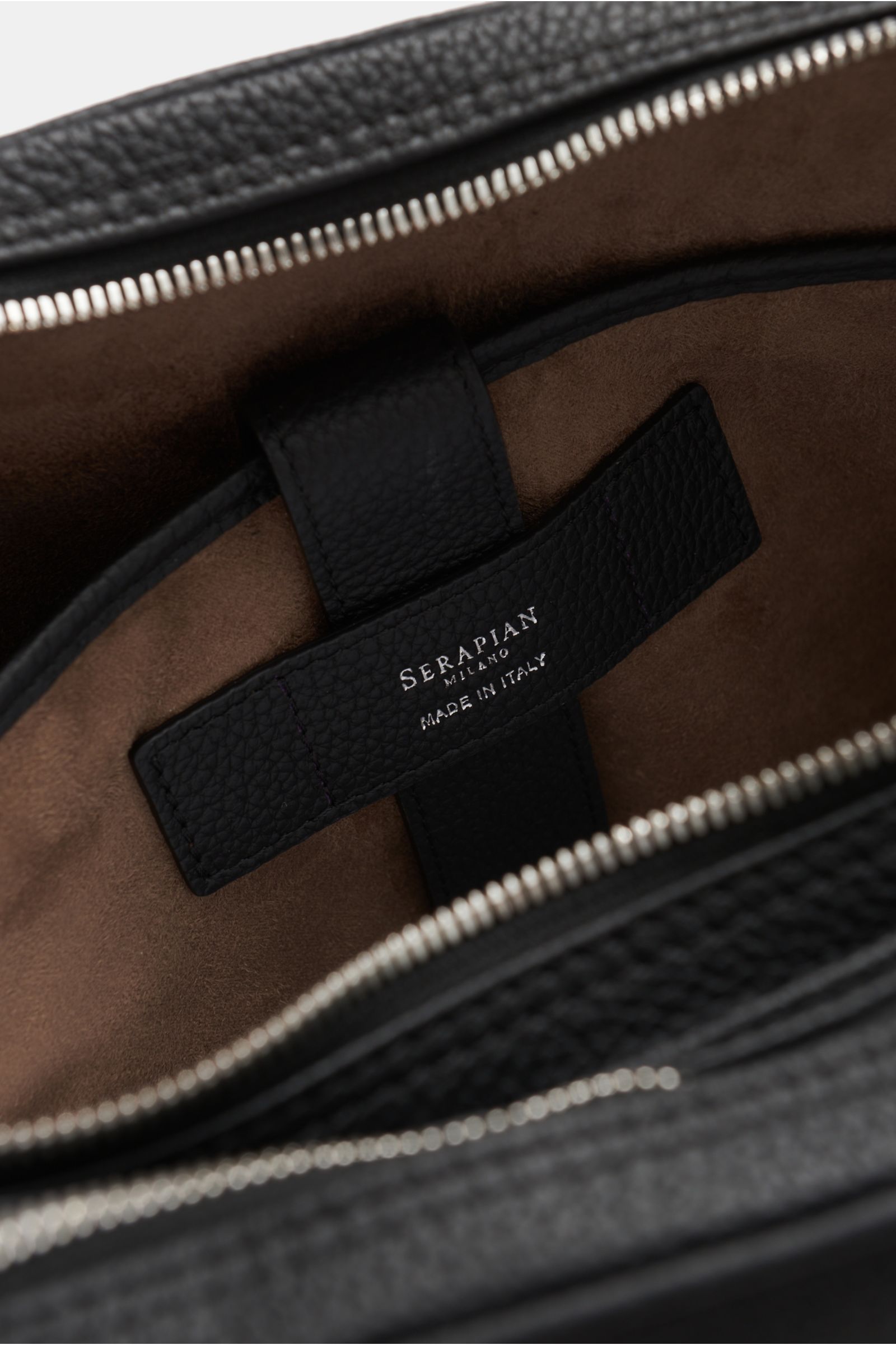 Serapian Aktentasche schwarz, Innenansicht von oben, markant genarbtes Kalbleder, weiches braunes Textilfutter, silberfarbener Reißverschluss, Logo-Prägung.