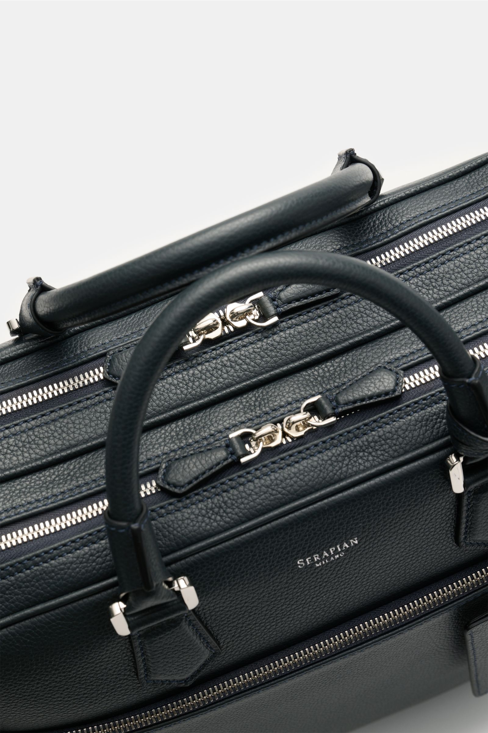 Close-up top view of the Serapian Aktentasche dark navy in markant genarbtes Kalbleder with silver hardware, robust handles, zippers, and logo detailing.