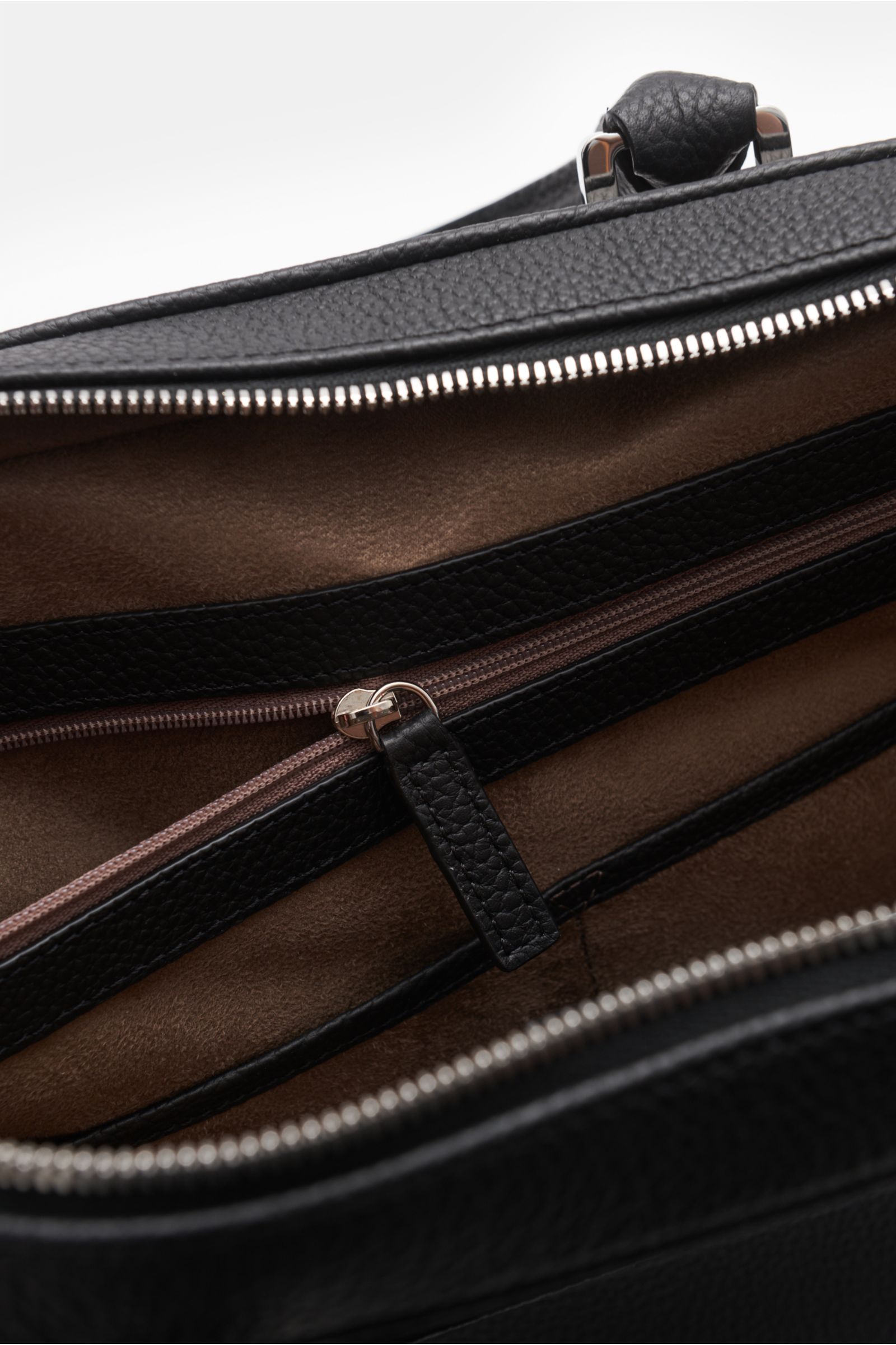 Close-up interior view of Serapian Aktentasche schwarz showing brown textile lining, a zipper pocket with black leather trim, and silver zipper hardware.