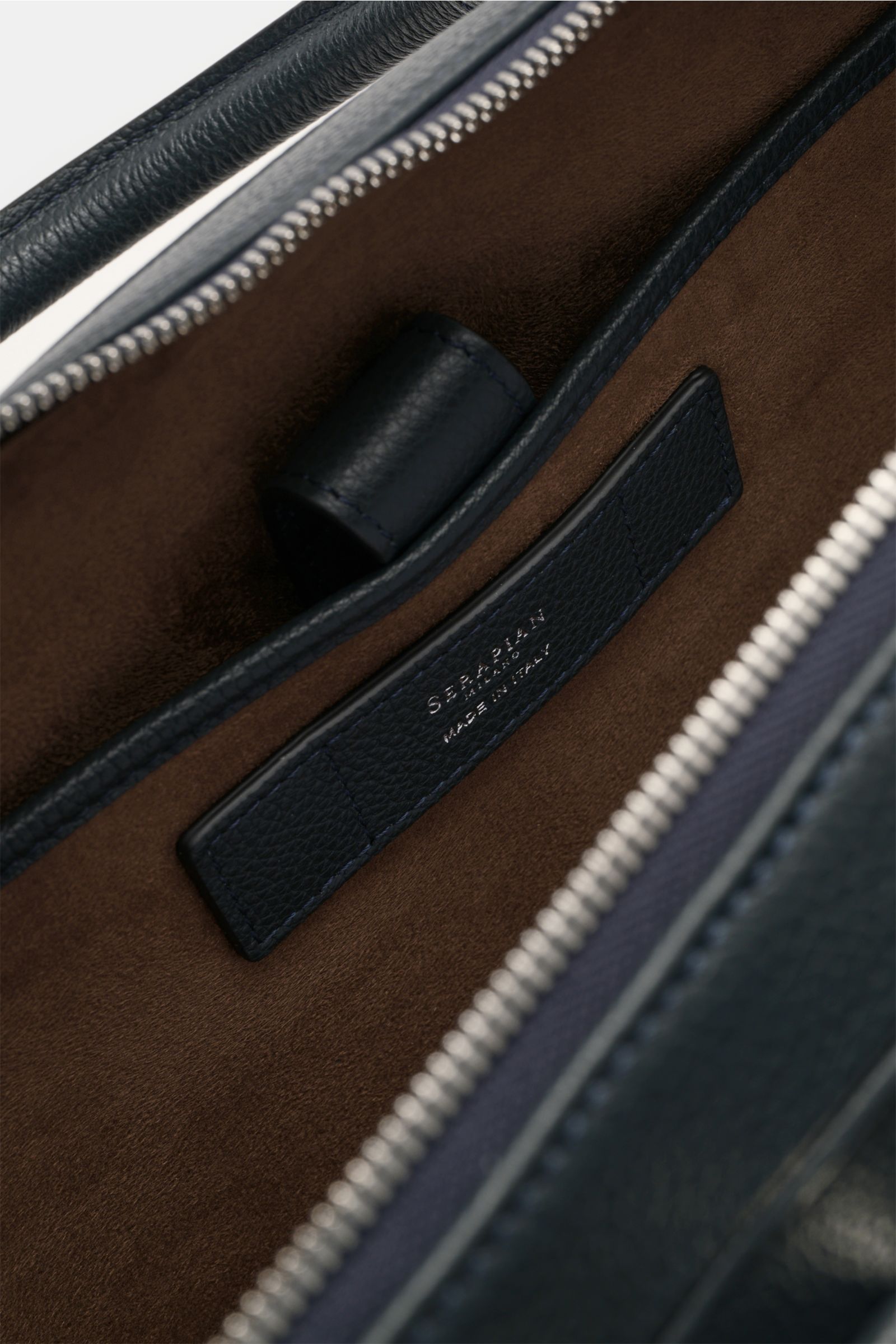 Nahaufnahme der geöffneten Serapian Aktentasche dark navy mit butterweichem, genarbtem Kalbleder, silberfarbenem Reißverschluss und braunem Textilfutter, Blick ins Hauptfach mit Logo-Prägung und Steckfächern.