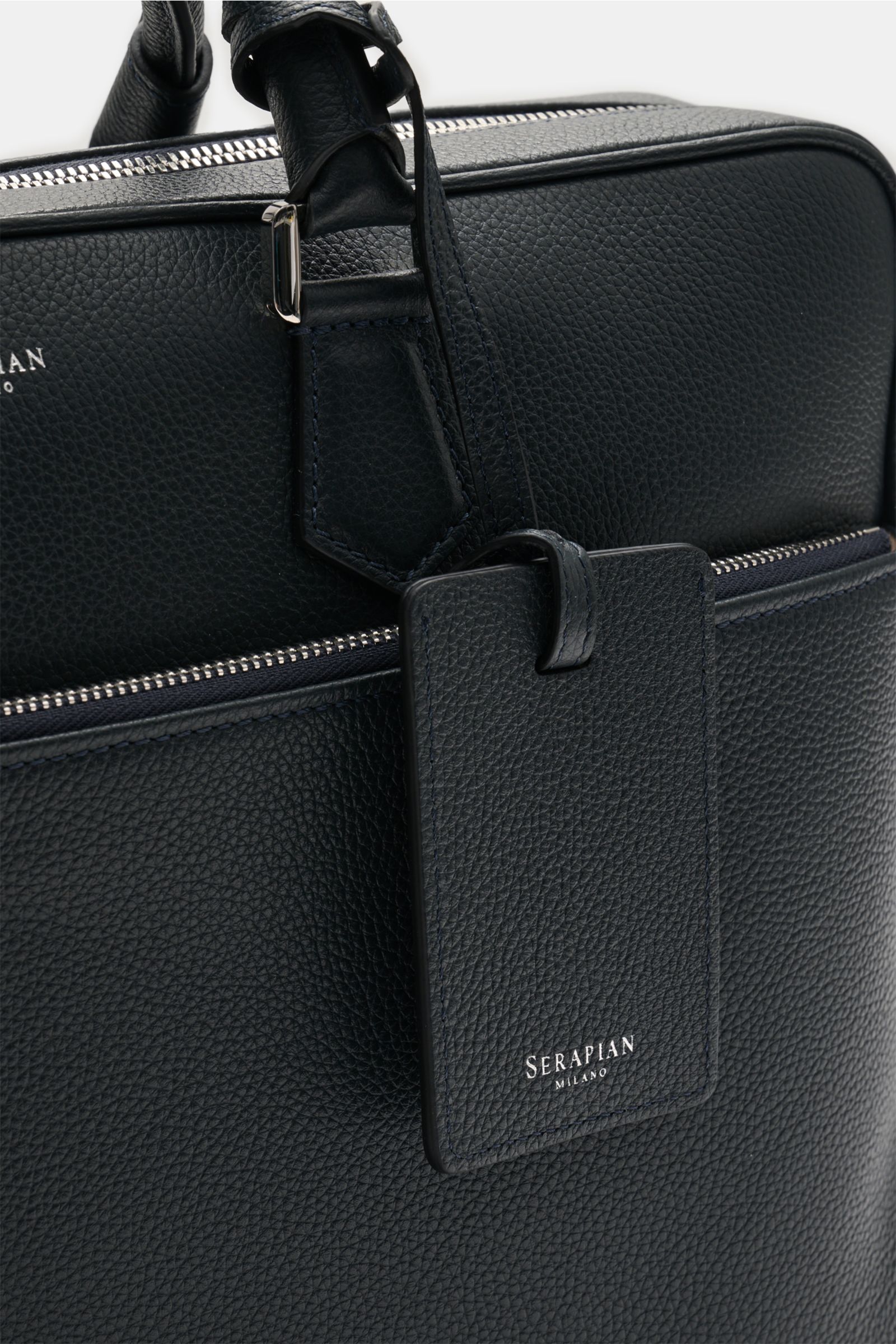Serapian Aktentasche dark navy aus markant genarbtem Kalbleder, silberner Hardware, abnehmbarem Gurt, frontal nah fotografiert.