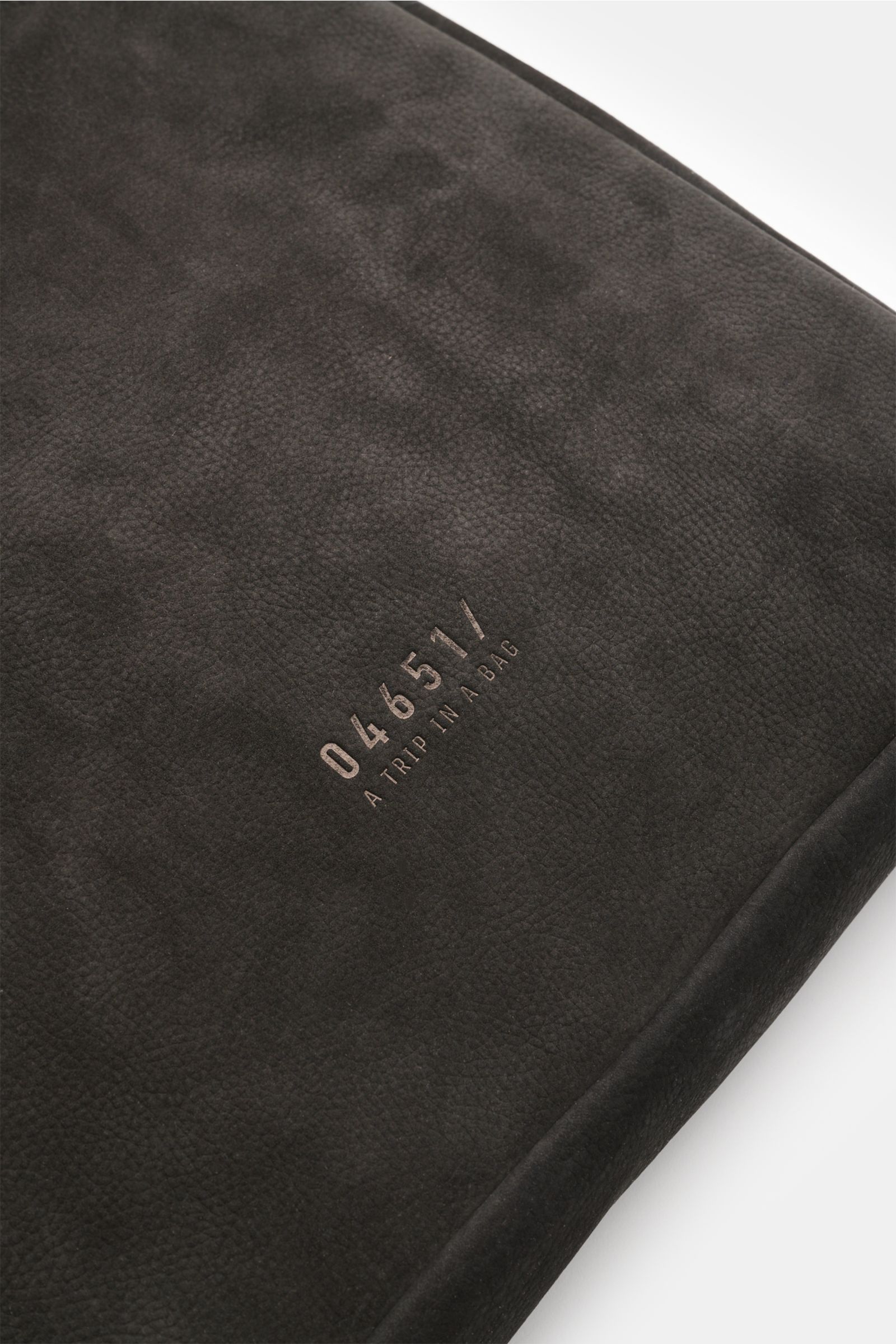 Close-up top view of the black 04651/ A trip in a bag Tote-Bag schwarz showing markant genarbtes Nubukleder with 04651/-Prägung on the front; geräumiger Allrounder with robuste Tragegriffe, geräumiges Hauptfach, Innenfach mit Reißverschluss, Laptopfach, a