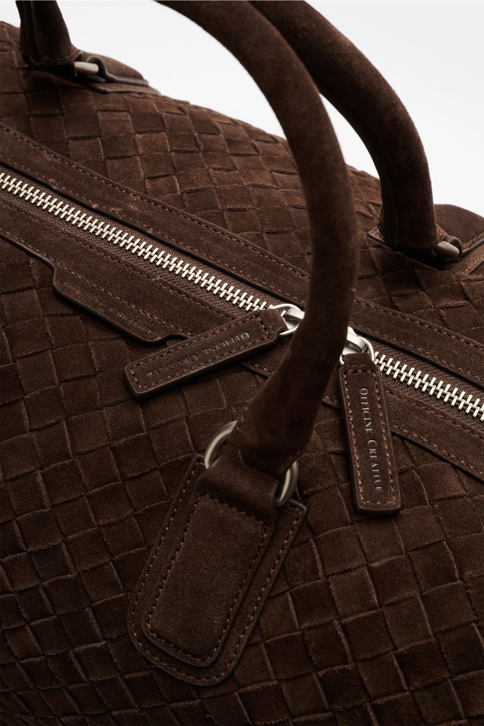 Nahaufnahme des Officine Creative Weekender dunkelbraun aus handgewebtem Veloursleder mit robusten Tragegriffen und silberfarbenem Zwei-Wege-Reißverschluss.